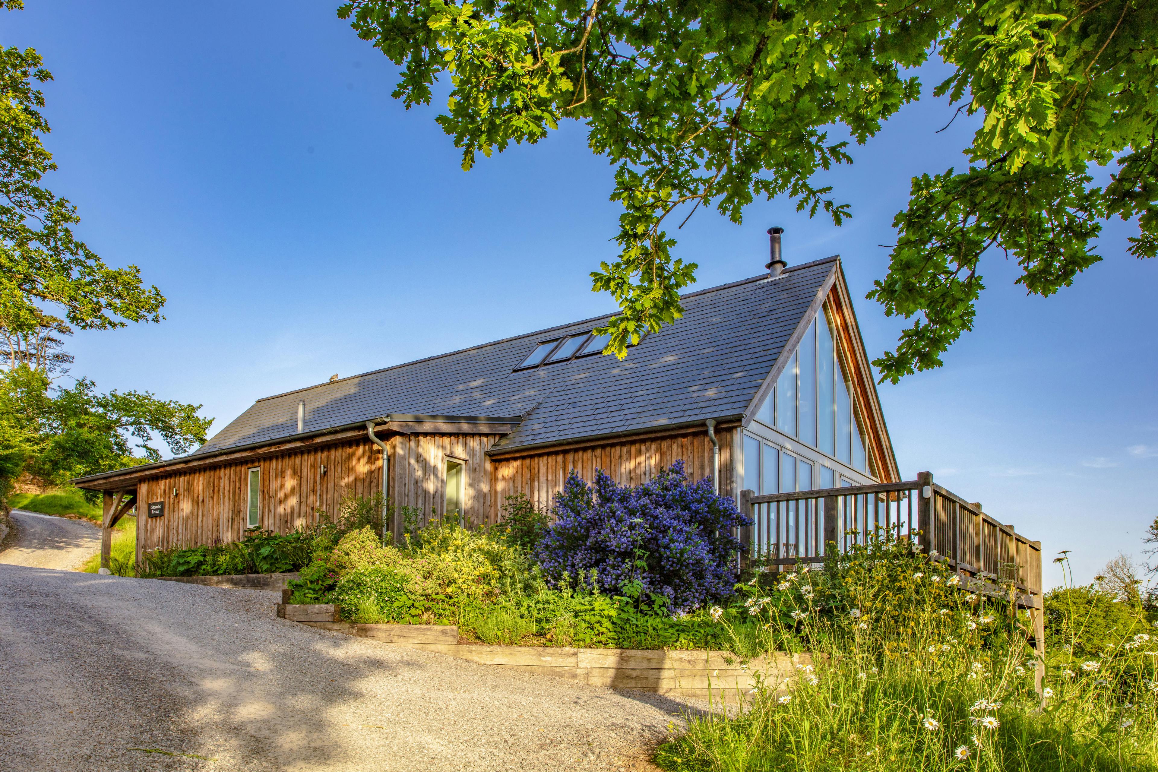 A timber clad oak framed home with a glazed gable end and a balcony in the countryside
