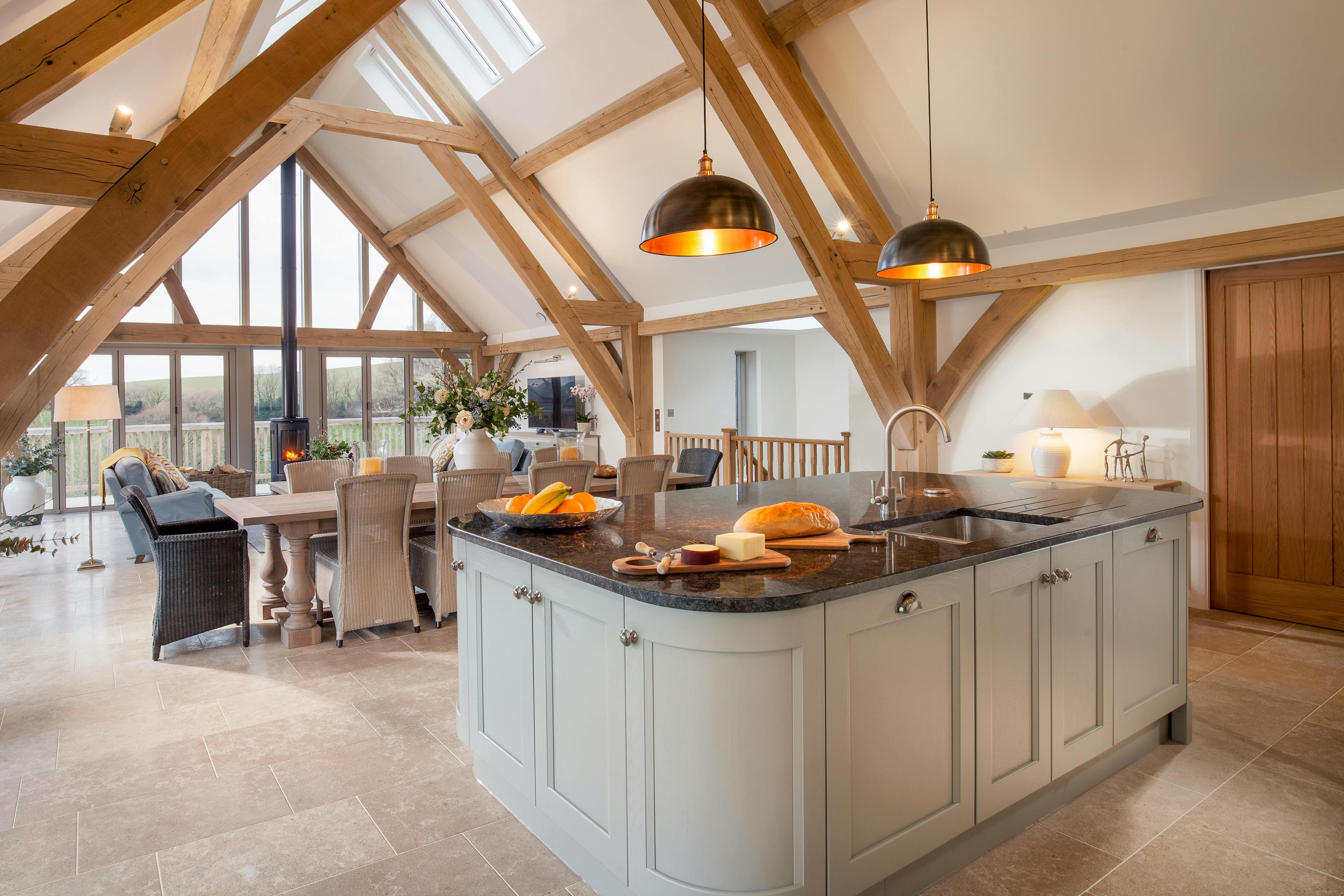 A kitchen island, dining area and sofa area in a vaulted an oak framed open plan living area