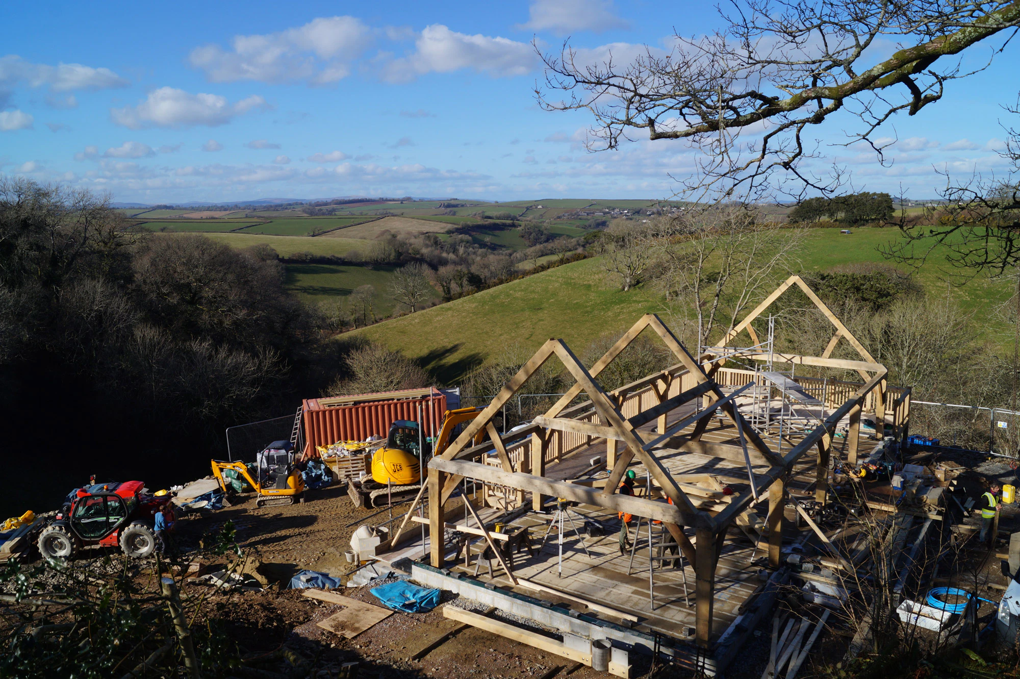 An oak frame being installed on a steep slope in the countryside