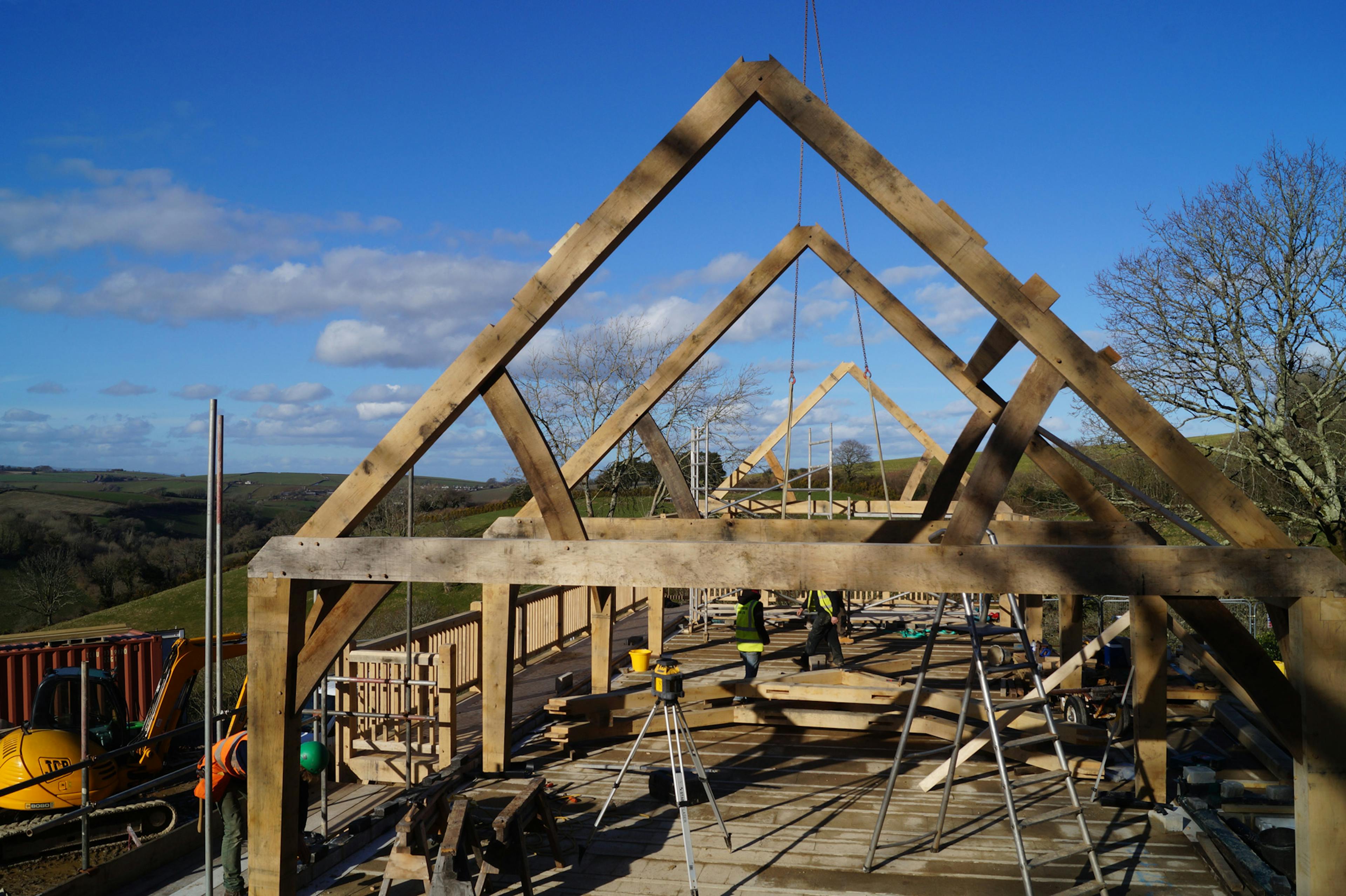 An oak frame being installed on a steep slope in the countryside