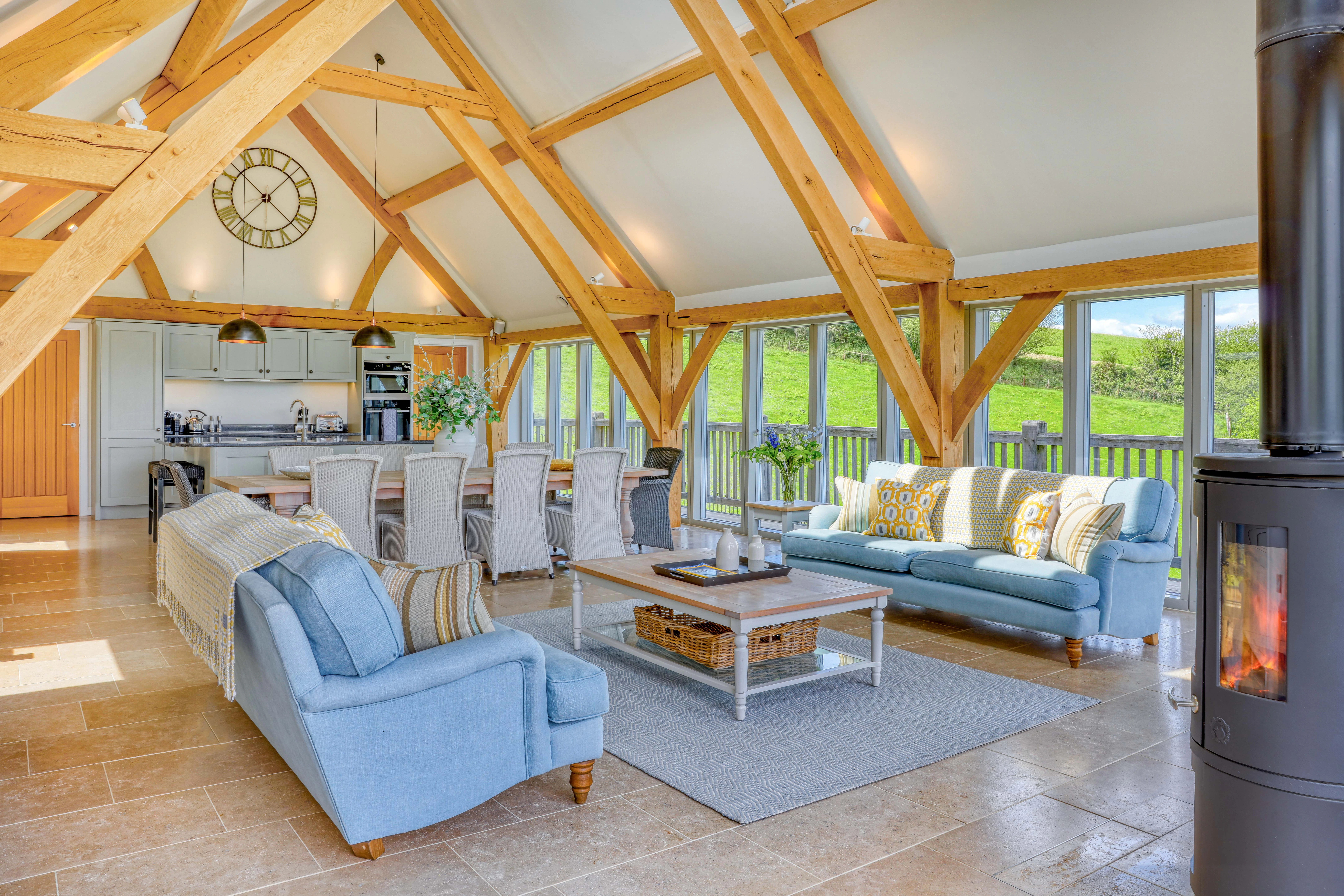 A sitting area with sofas and log burner, a dining area and kitchen in a vaulted an oak framed open plan living area