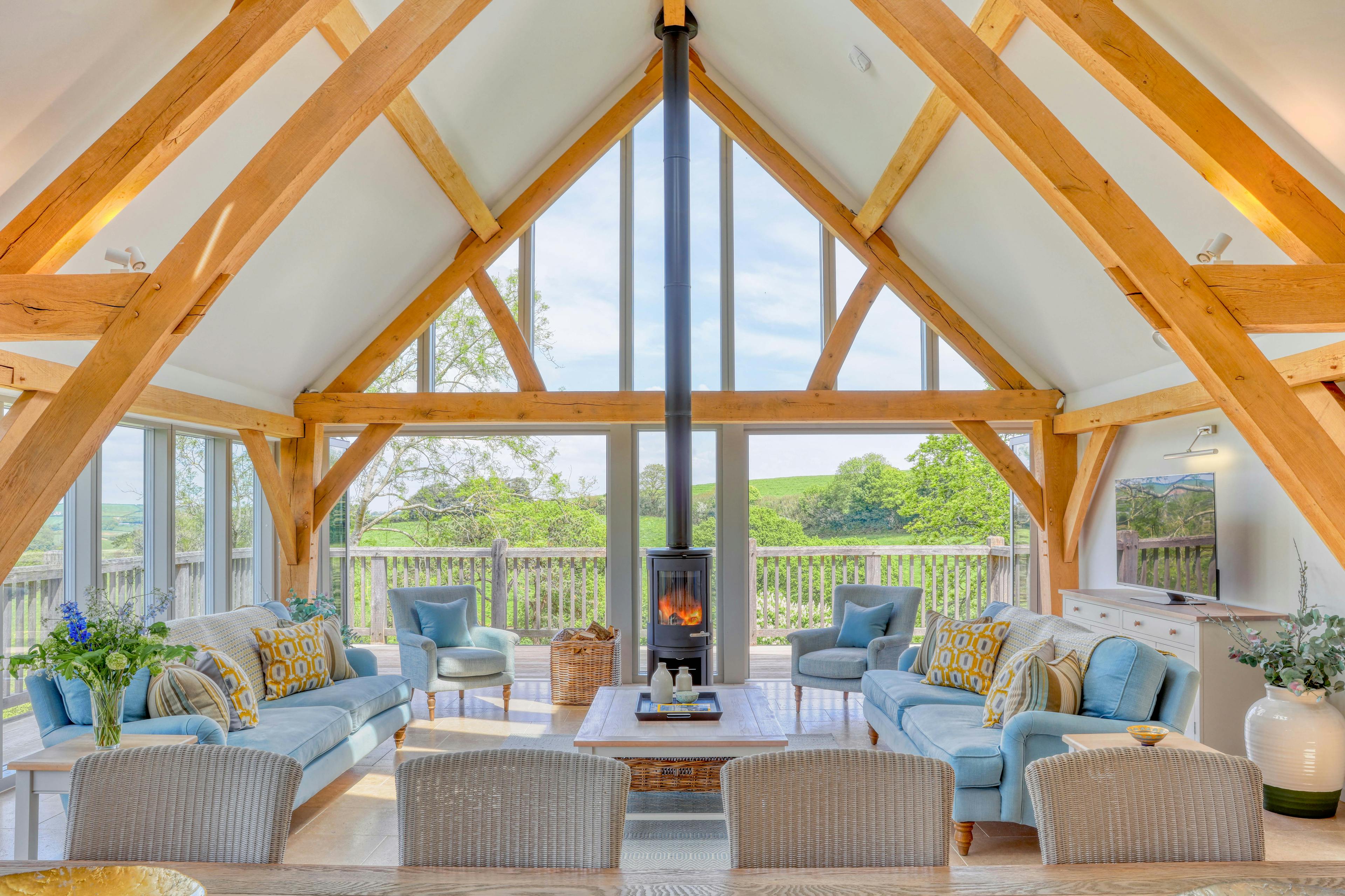 A dining table and sitting area with sofas and log burner in a vaulted an oak framed open plan living area