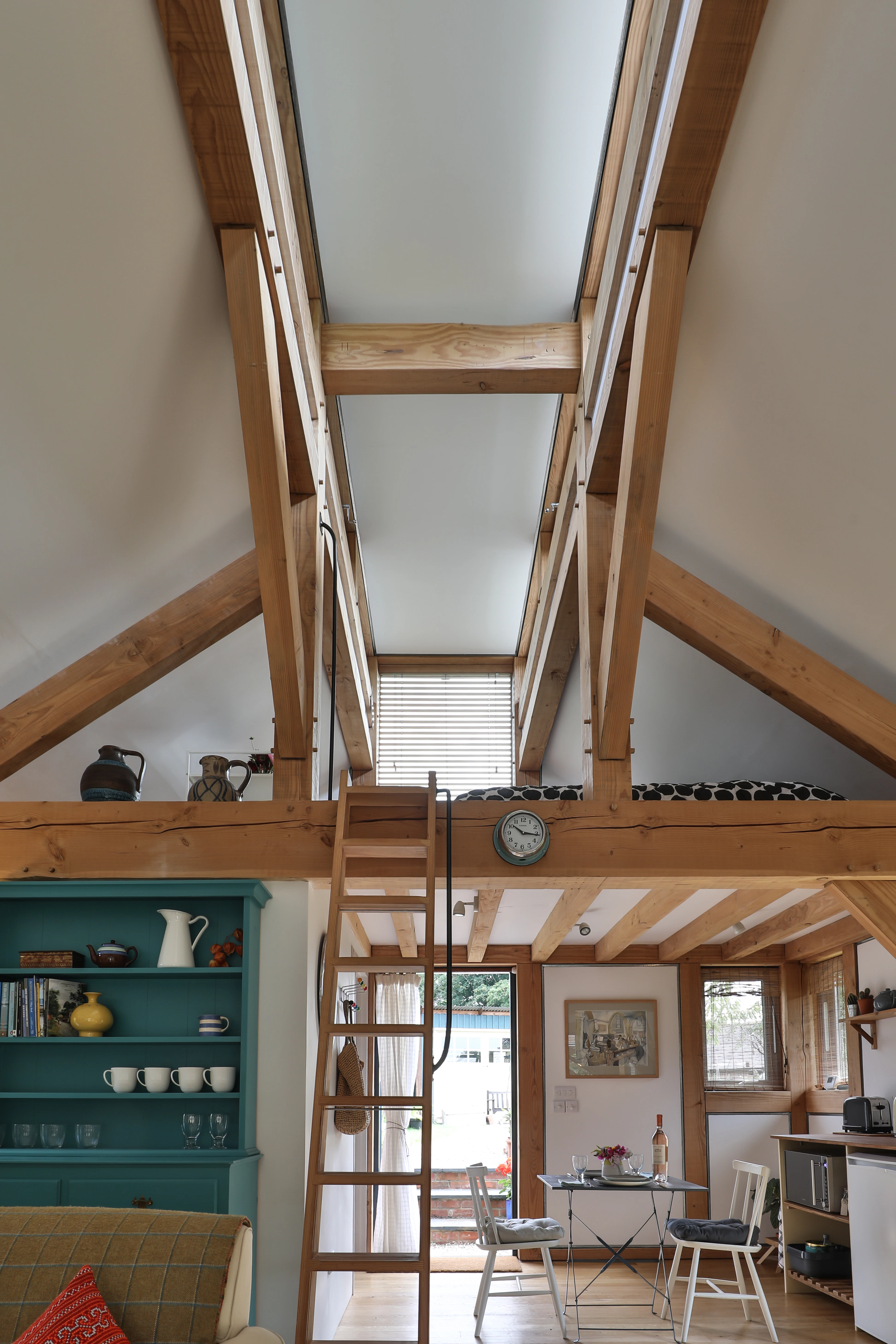 A wooden ladder leads to a mezzanine sleeping area in a Douglas fir framed annex