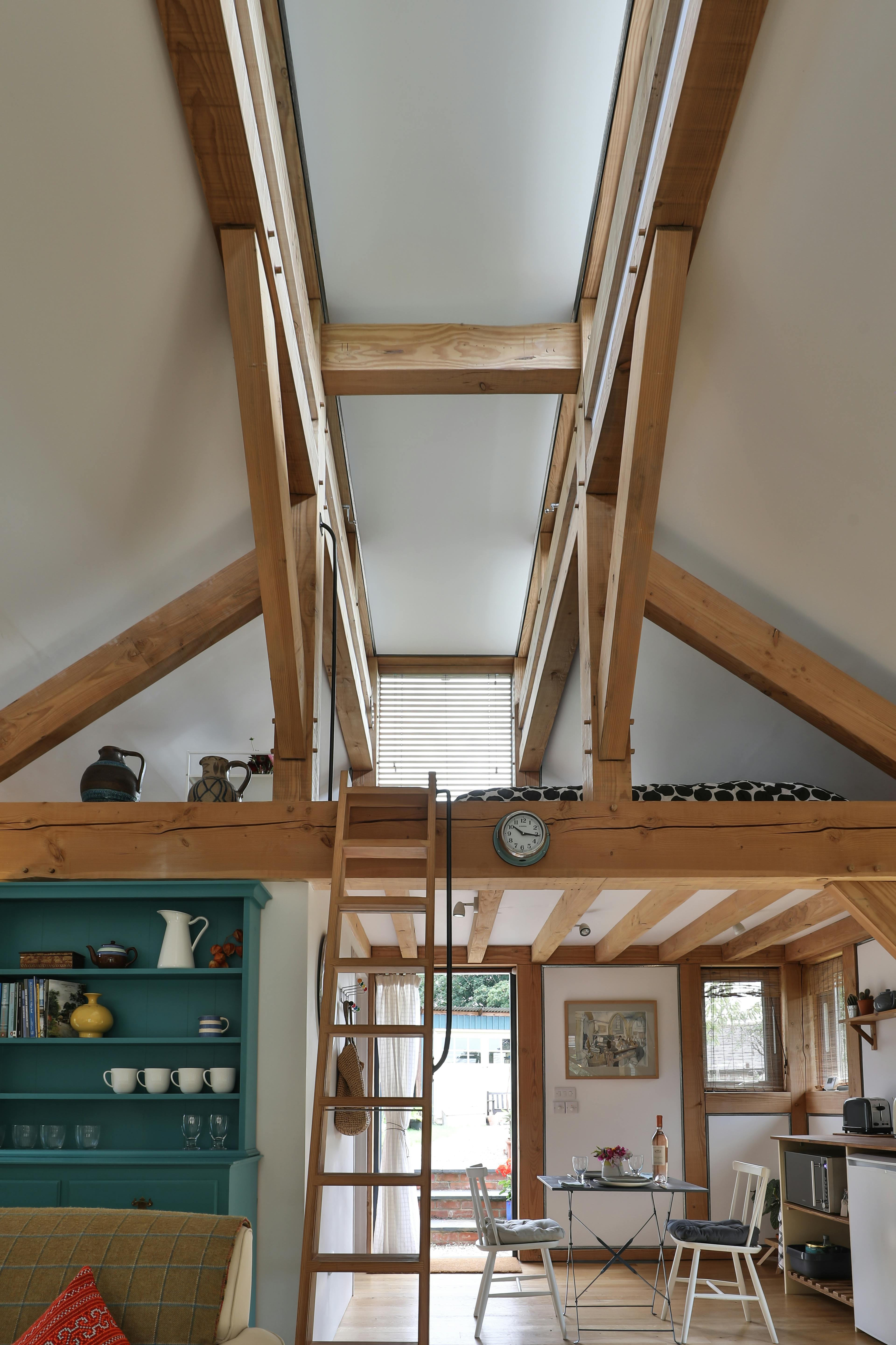 A wooden ladder leads to a mezzanine sleeping area in a Douglas fir framed annex