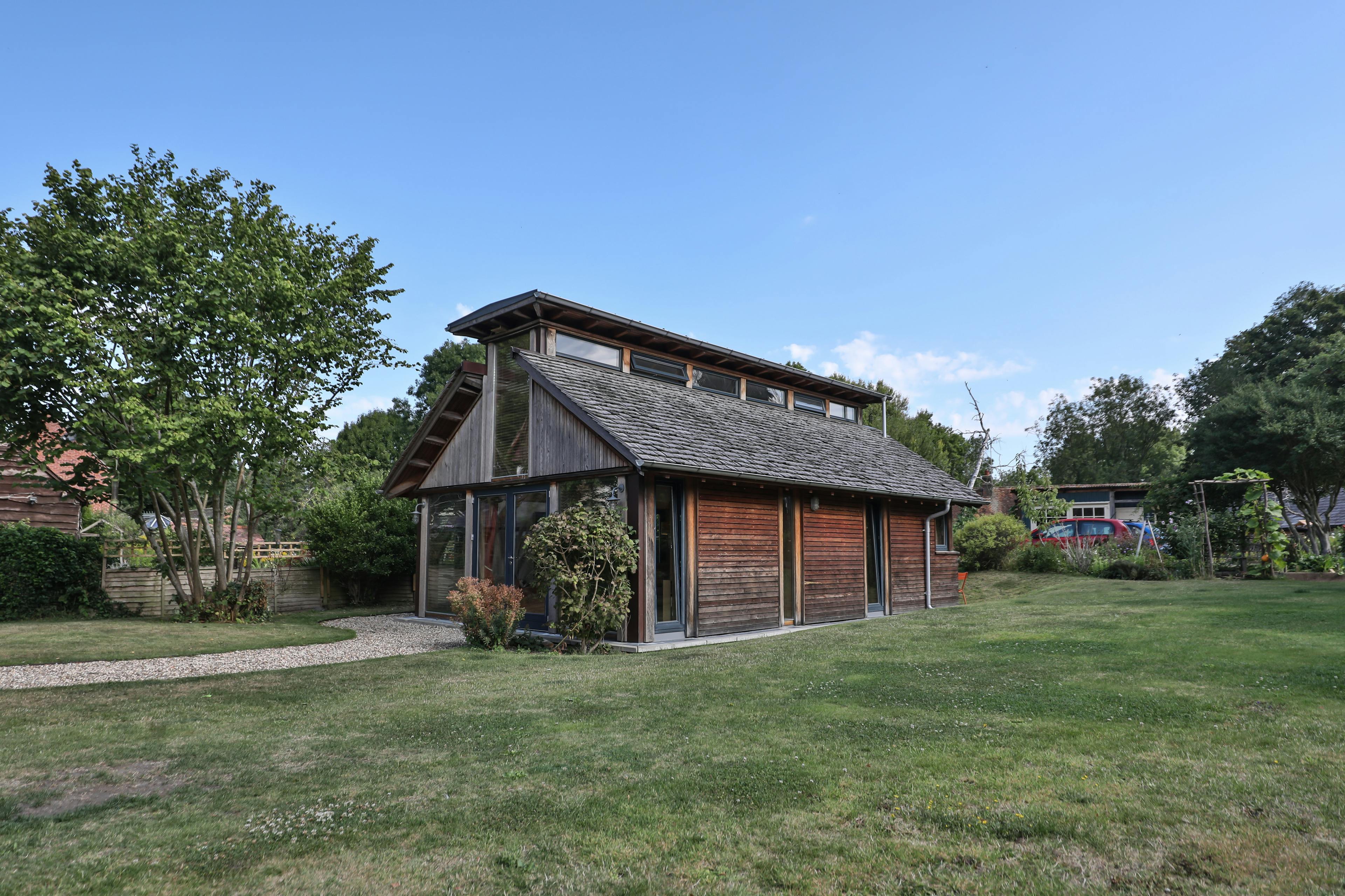 The back and side of a Douglas fir framed building with cedar cladding and oak shingles with a garden around it