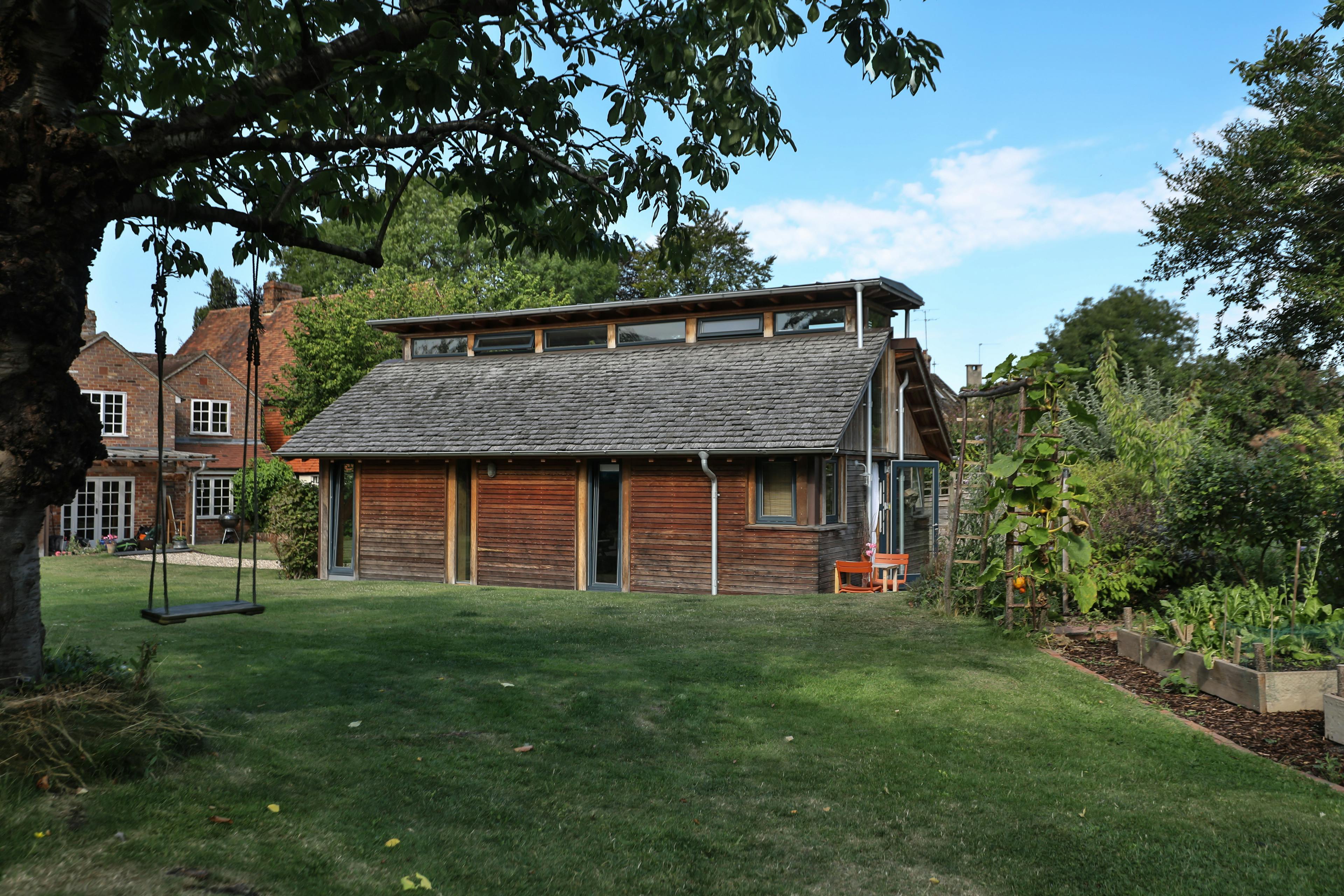 The side of a Douglas fir framed building with cedar cladding and oak shingles with a garden around it