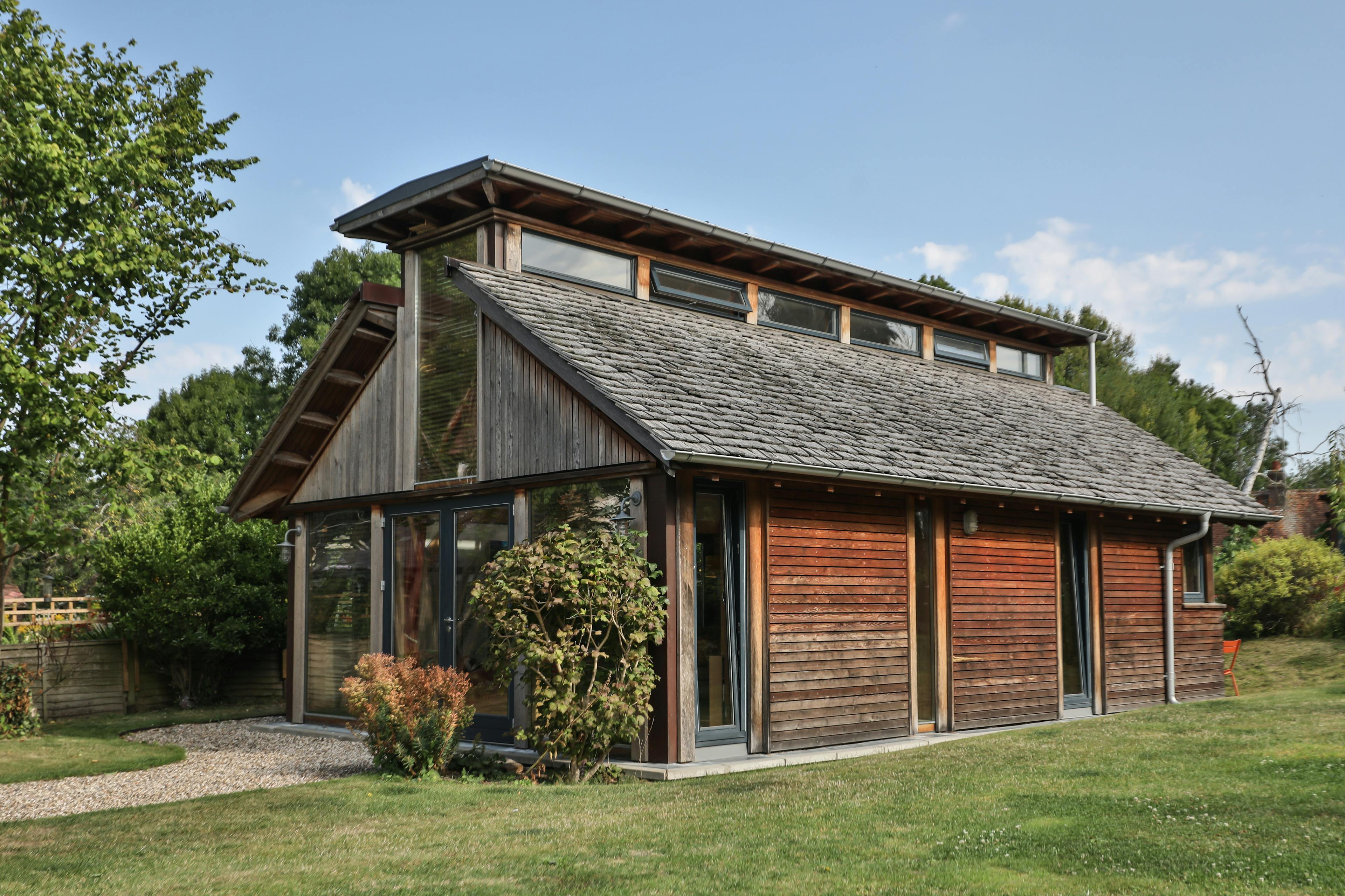The back and side of a Douglas fir framed building with cedar cladding and oak shingles with a garden around it