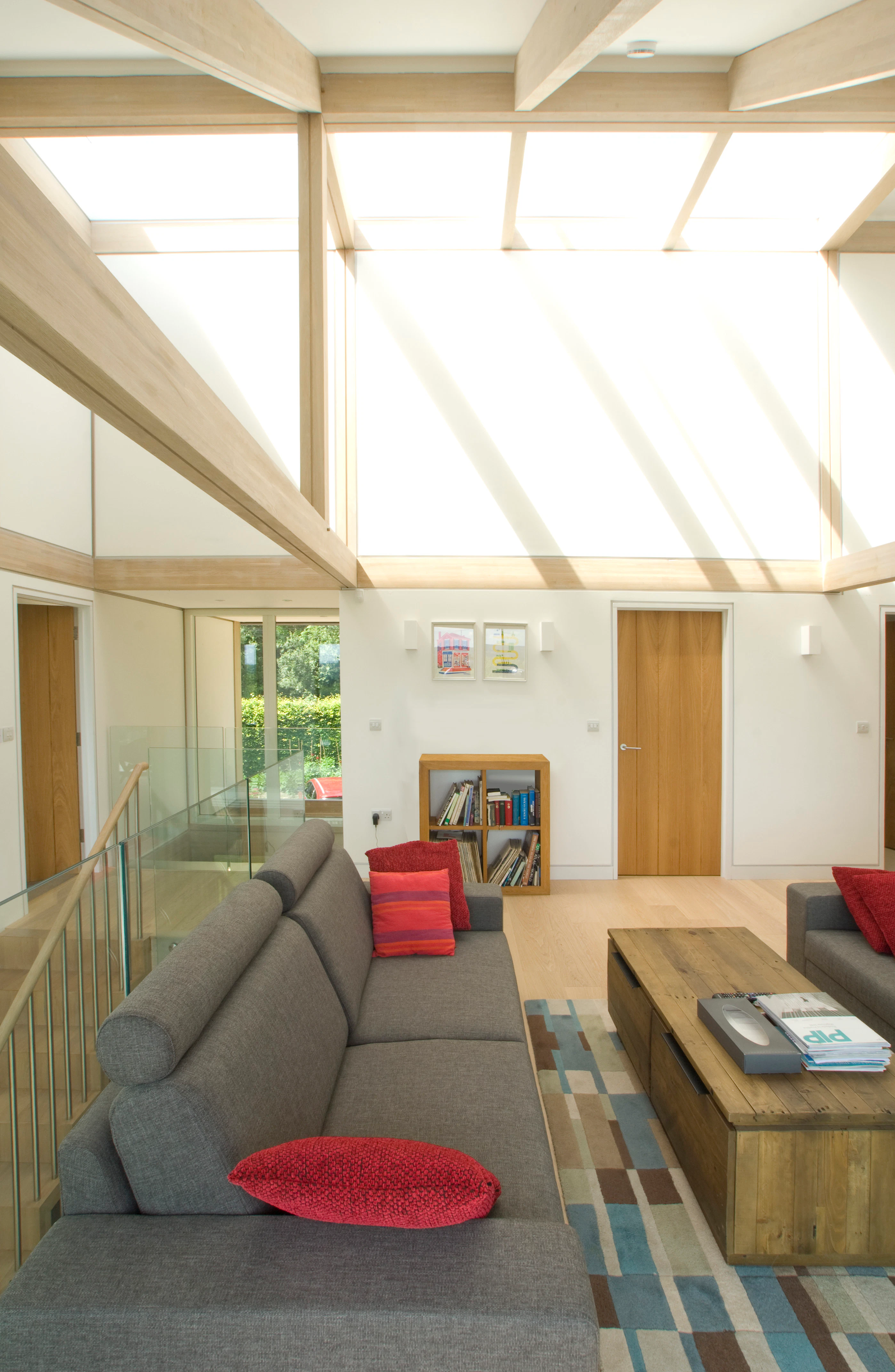 Sunlight shines down from rooflights onto a mezzanine living room with sofas in an oak glulam framed house