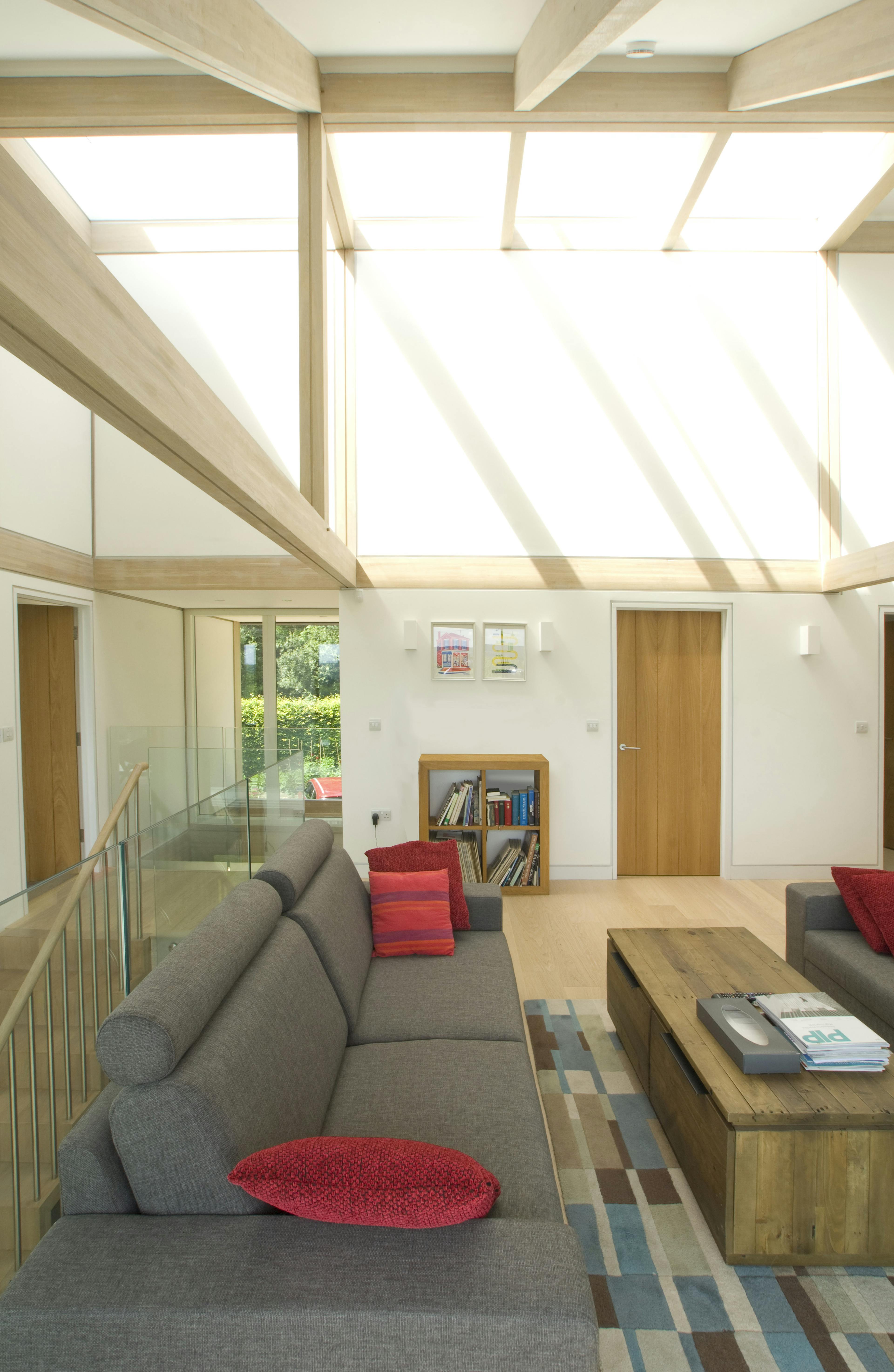 Sunlight shines down from rooflights onto a mezzanine living room with sofas in an oak glulam framed house