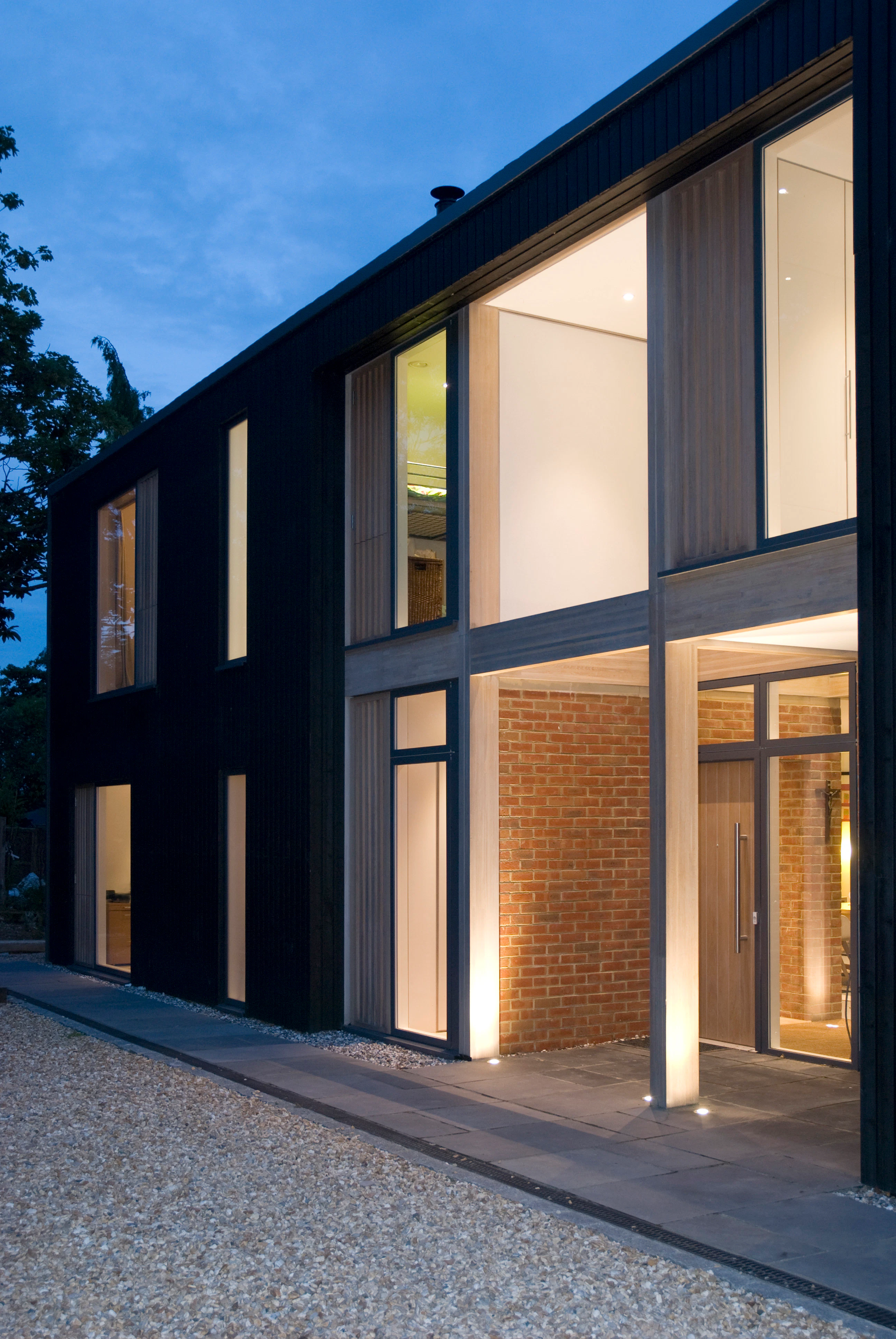 Lights shines from large glazed windows and doors of the front of a large house at twilight