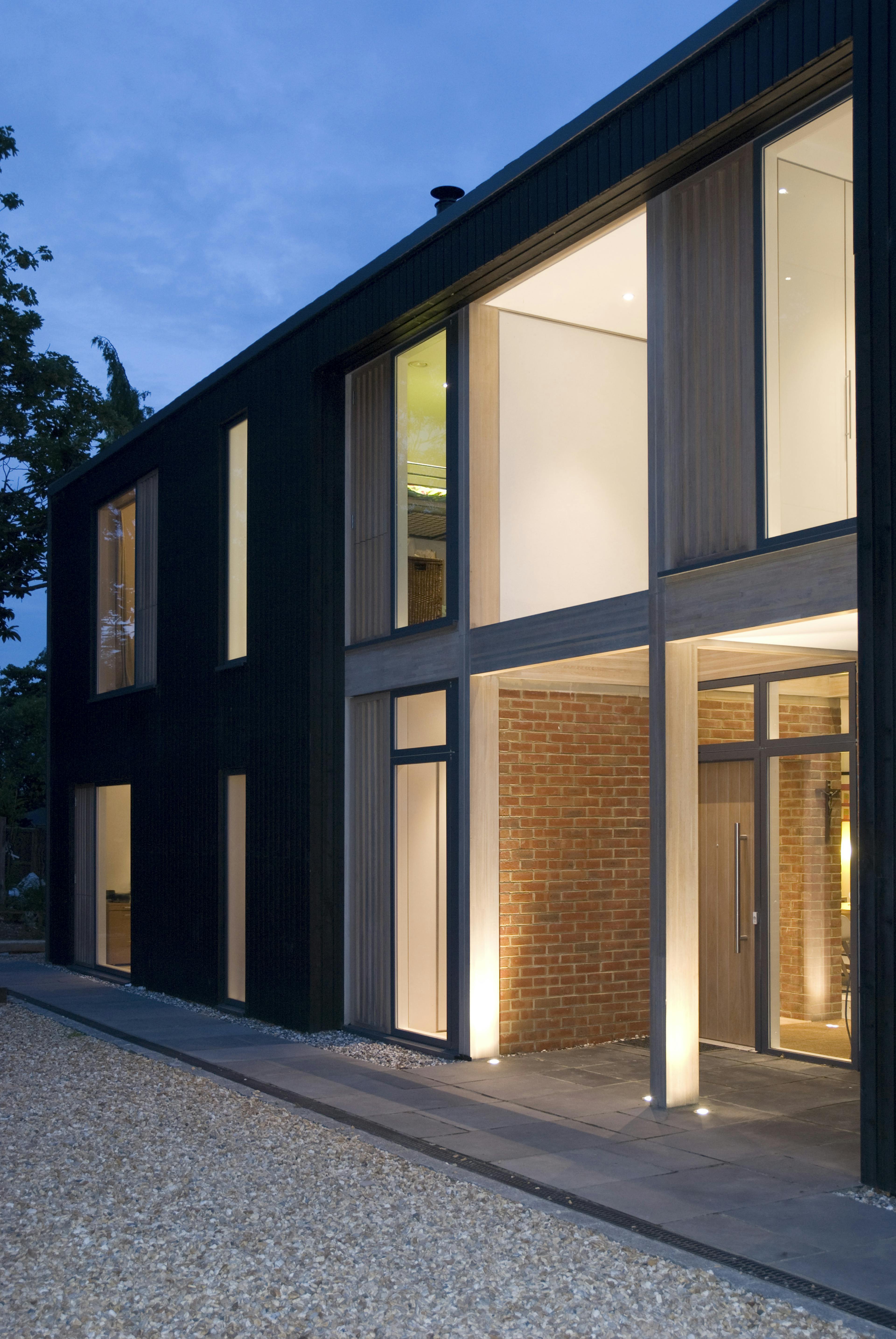 Lights shines from large glazed windows and doors of the front of a large house at twilight