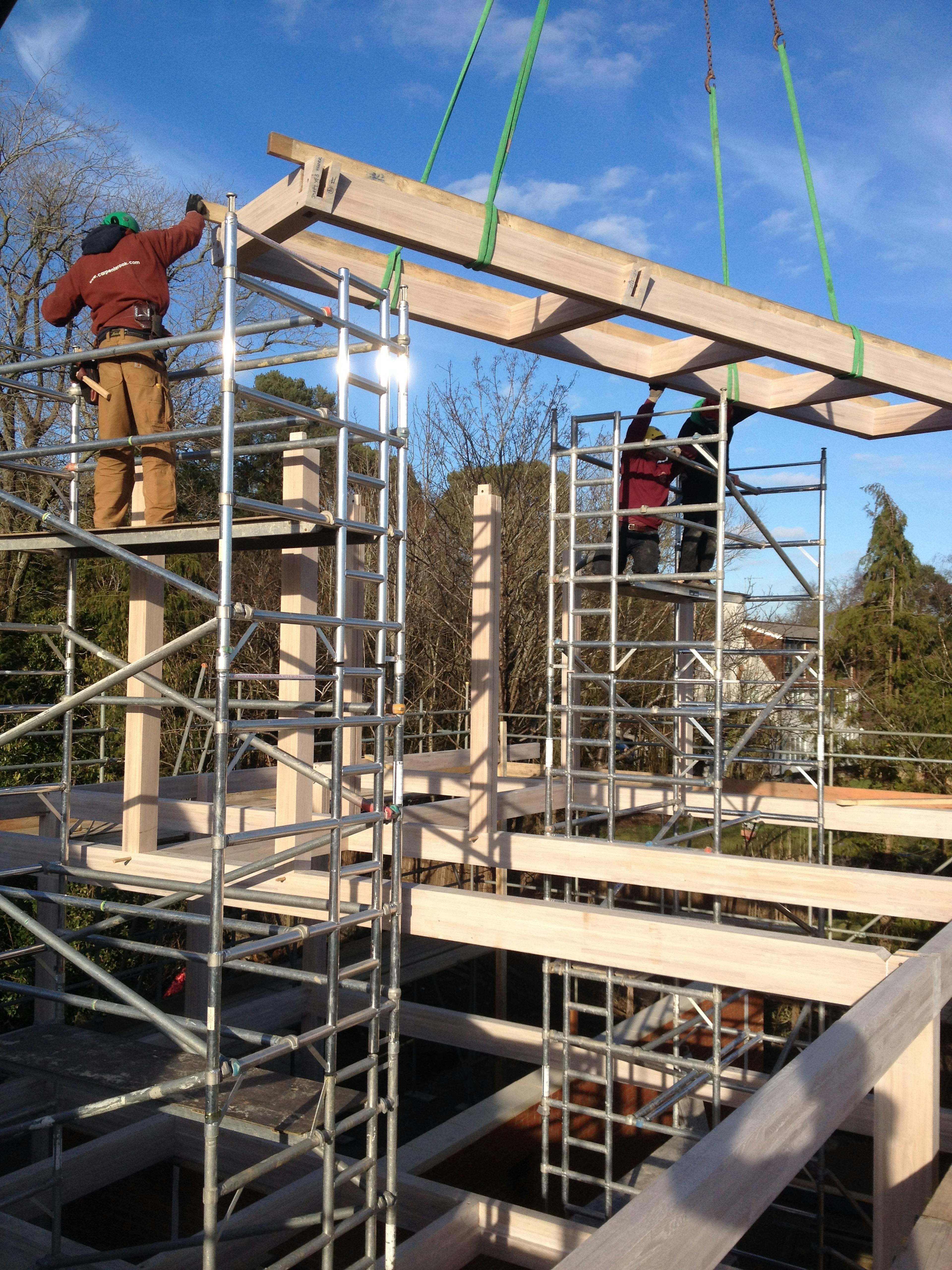 A section of a frame of an oak glulam house is lowered into place by a crane during construction