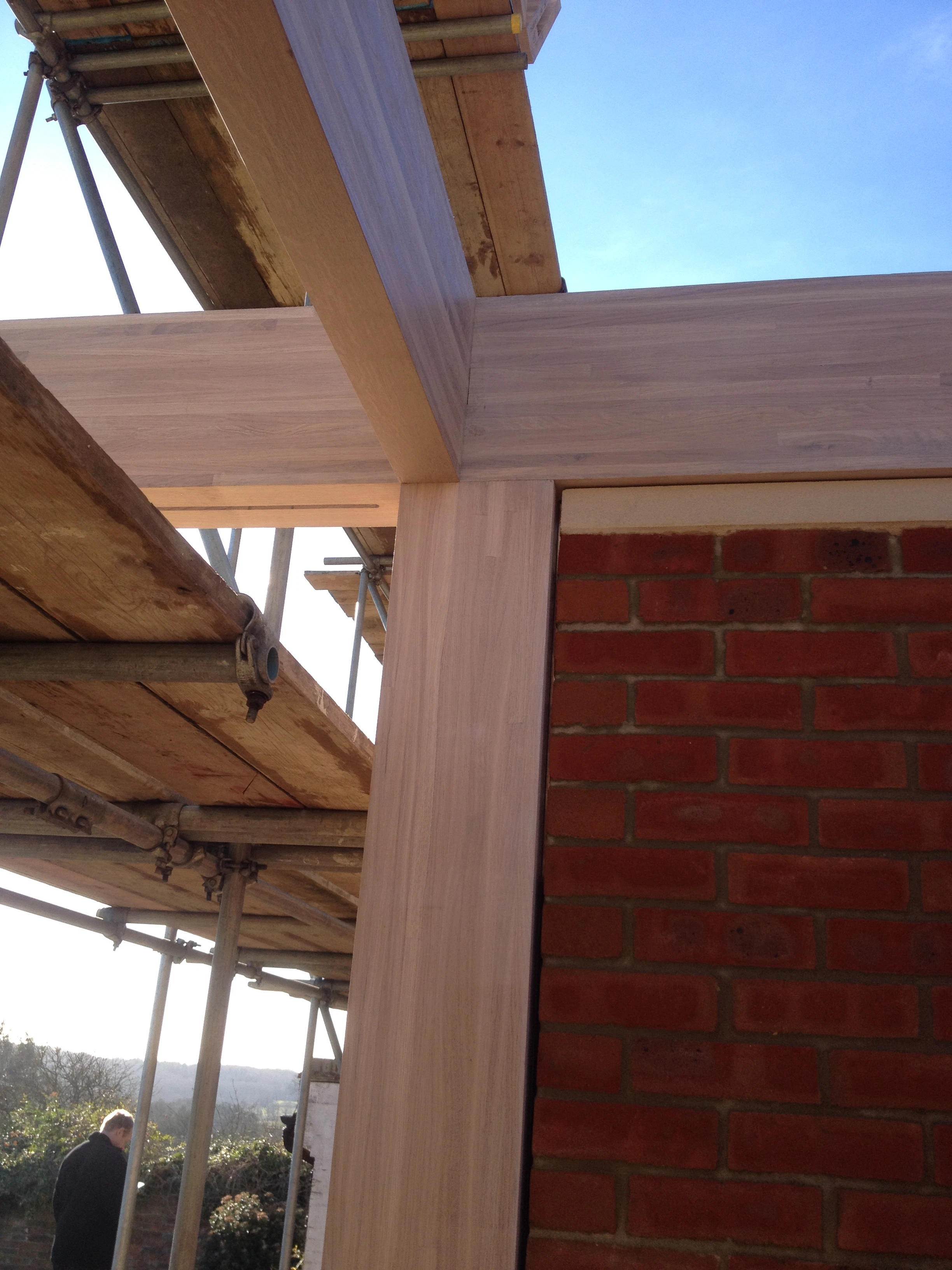 A join of an oak glulam frame beside a red brick wall during construction