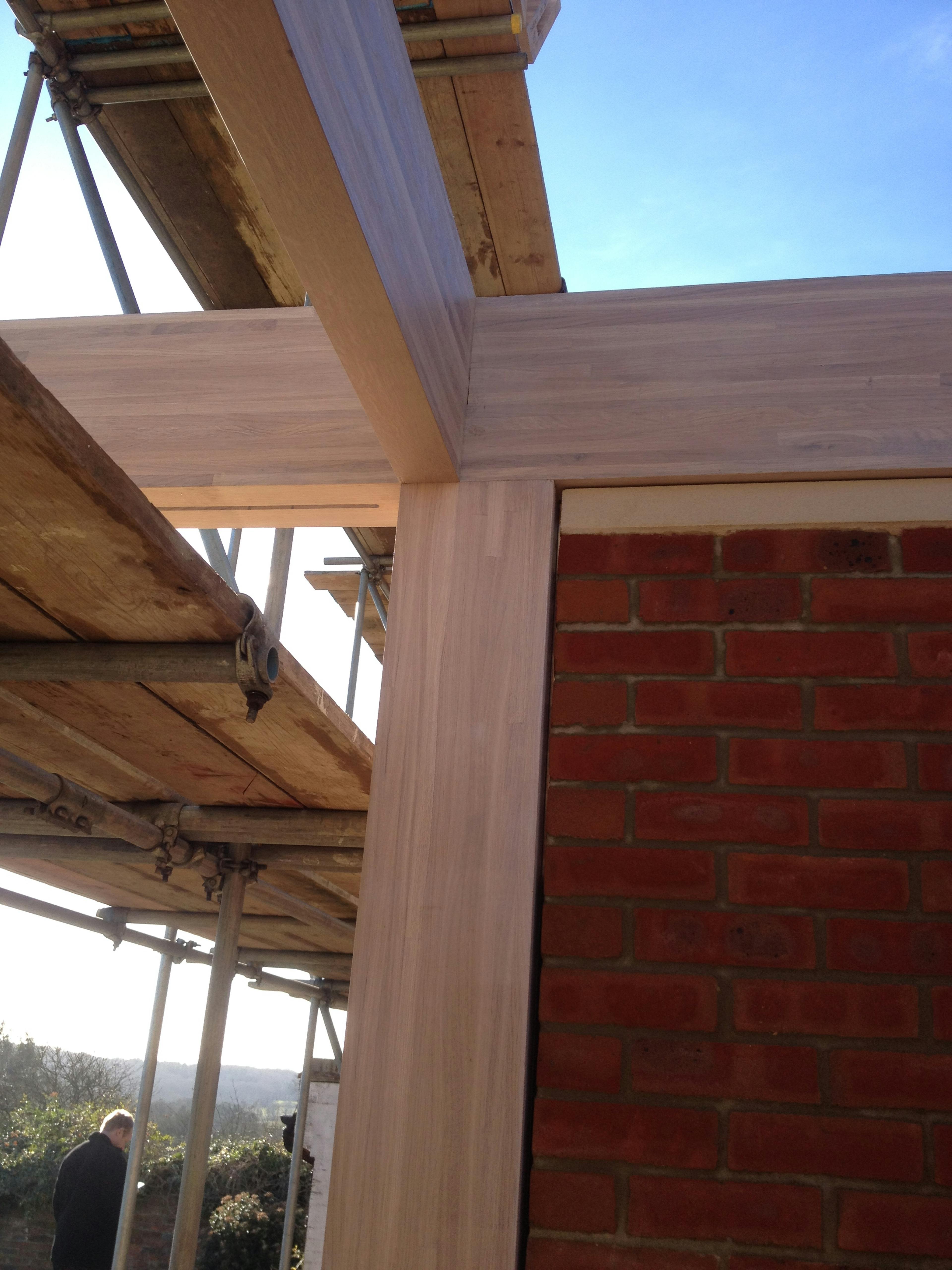 A join of an oak glulam frame beside a red brick wall during construction