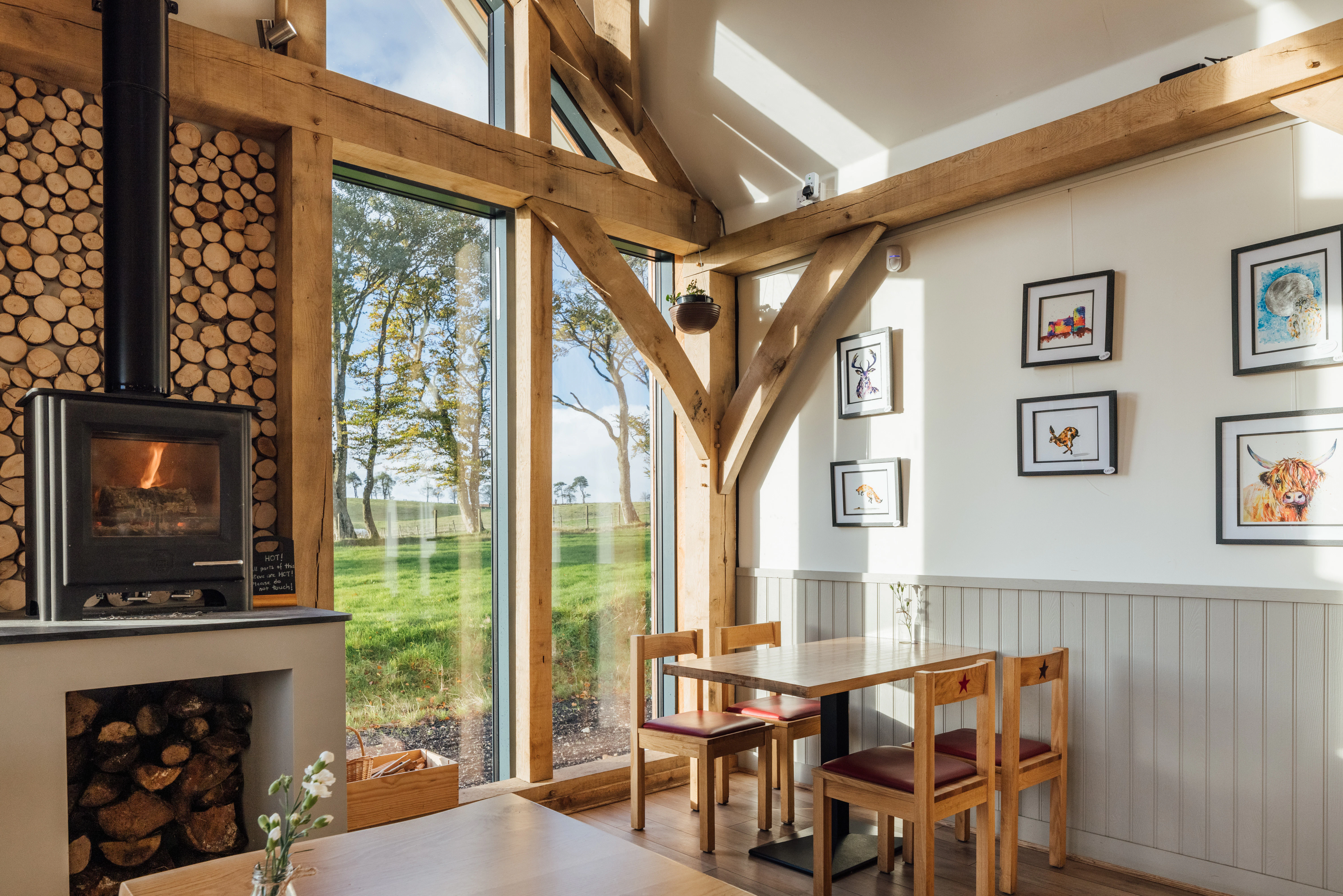 An oak framed cafe with a log burner and neatly stacked logs under a vaulted ceiling