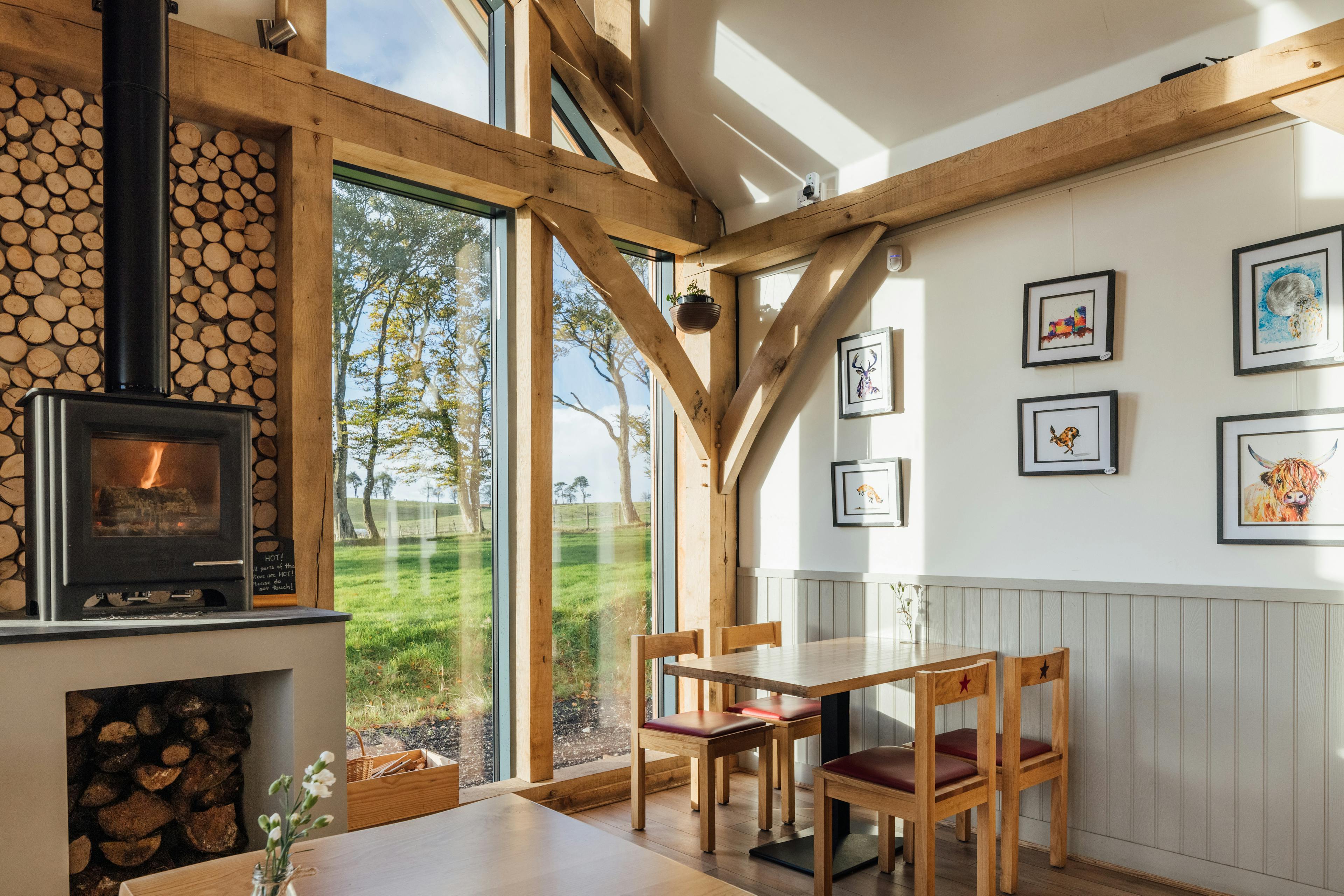 An oak framed cafe with a log burner and neatly stacked logs under a vaulted ceiling