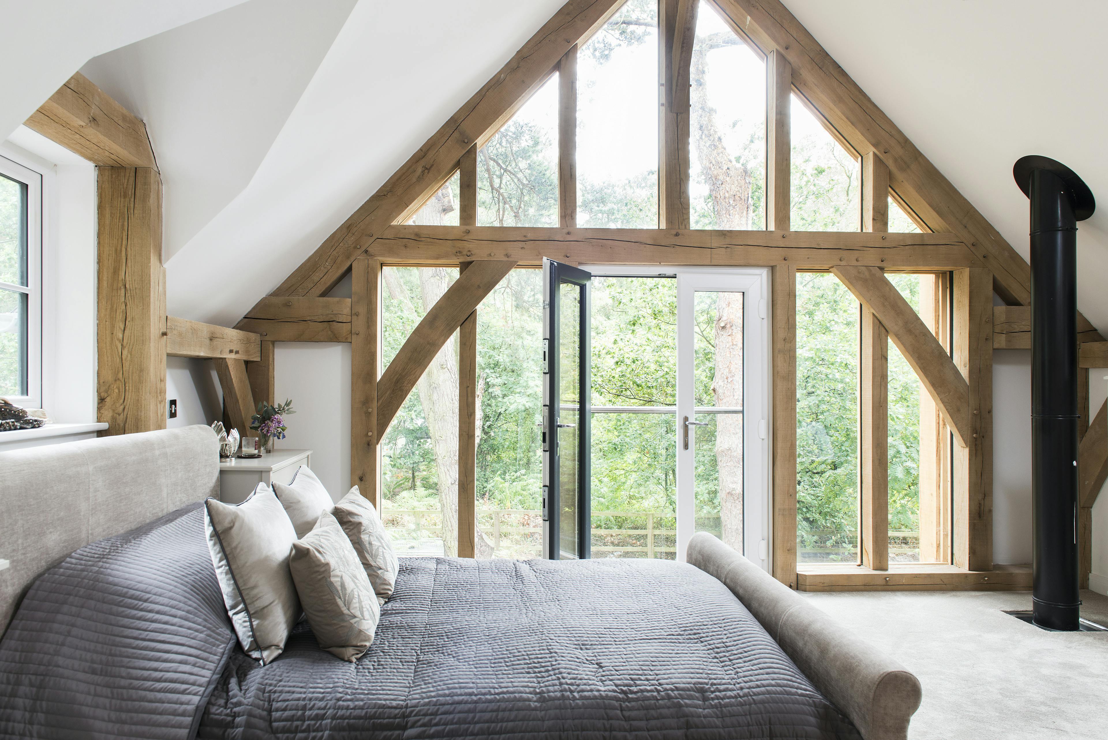 A large double bed in oak framed bedroom with an glazed gable end and French double doors opening out to the garden