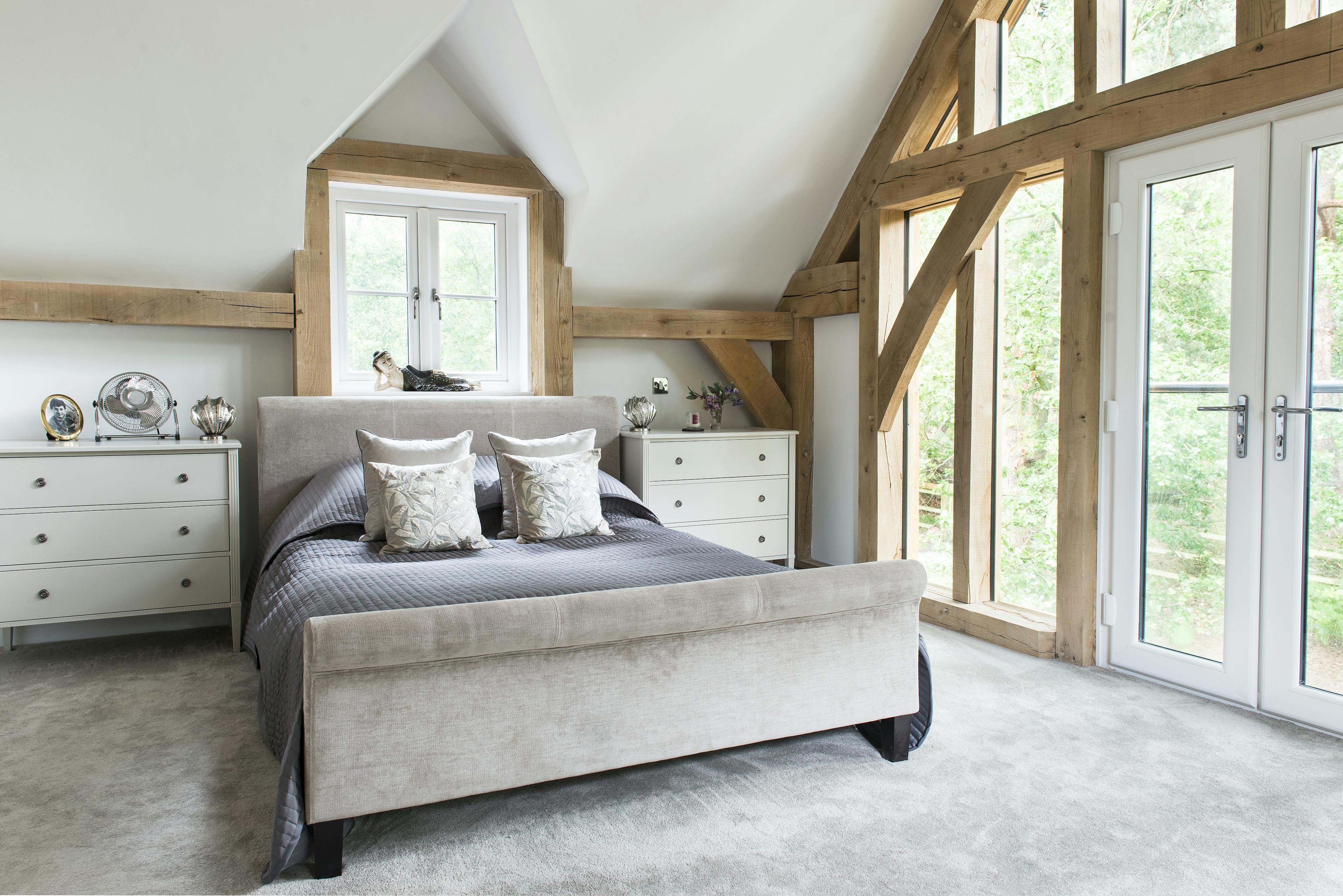 A large double bed in oak framed bedroom with an glazed gable end and French double doors opening out to the garden