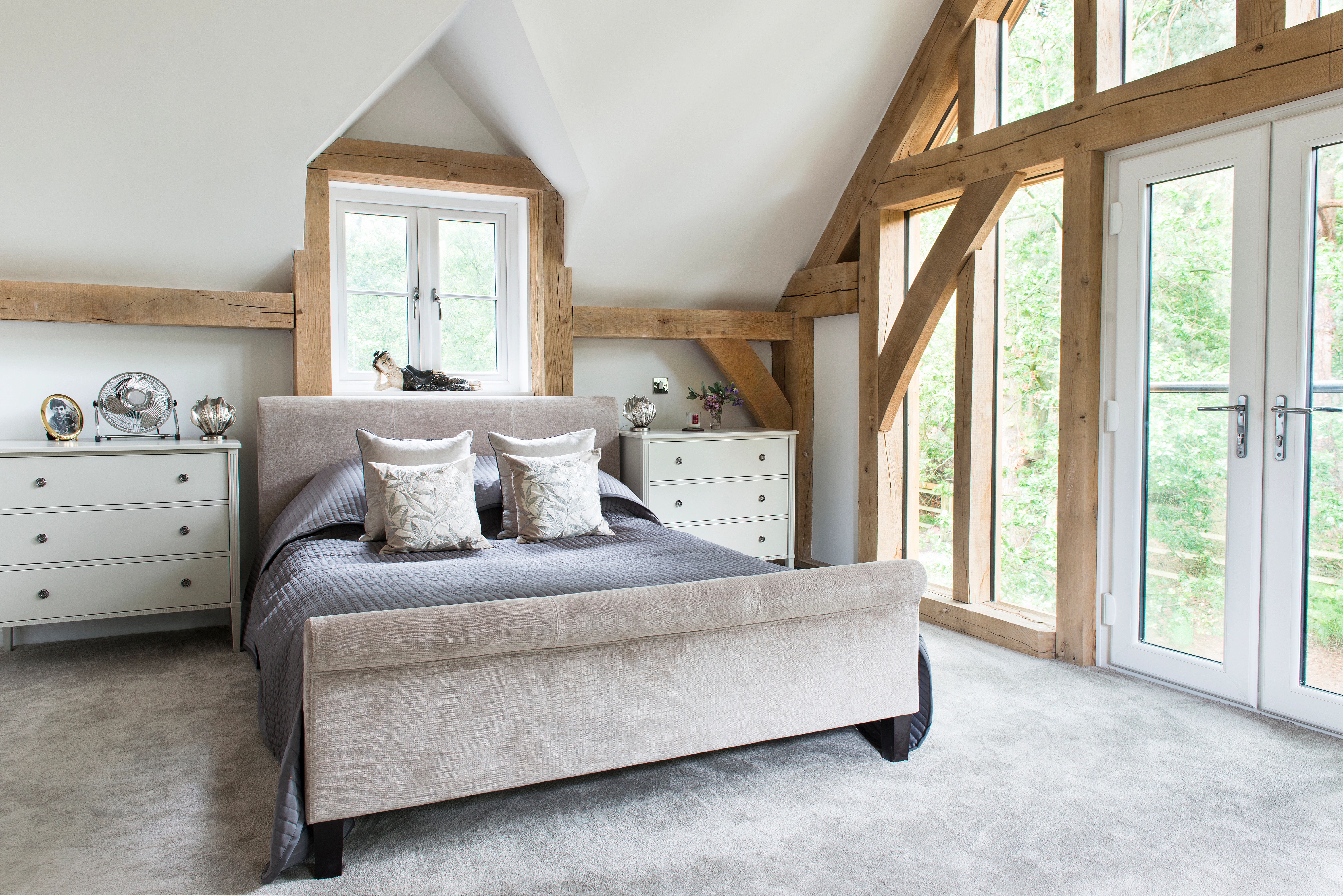 A large double bed in oak framed bedroom with an glazed gable end and French double doors opening out to the garden