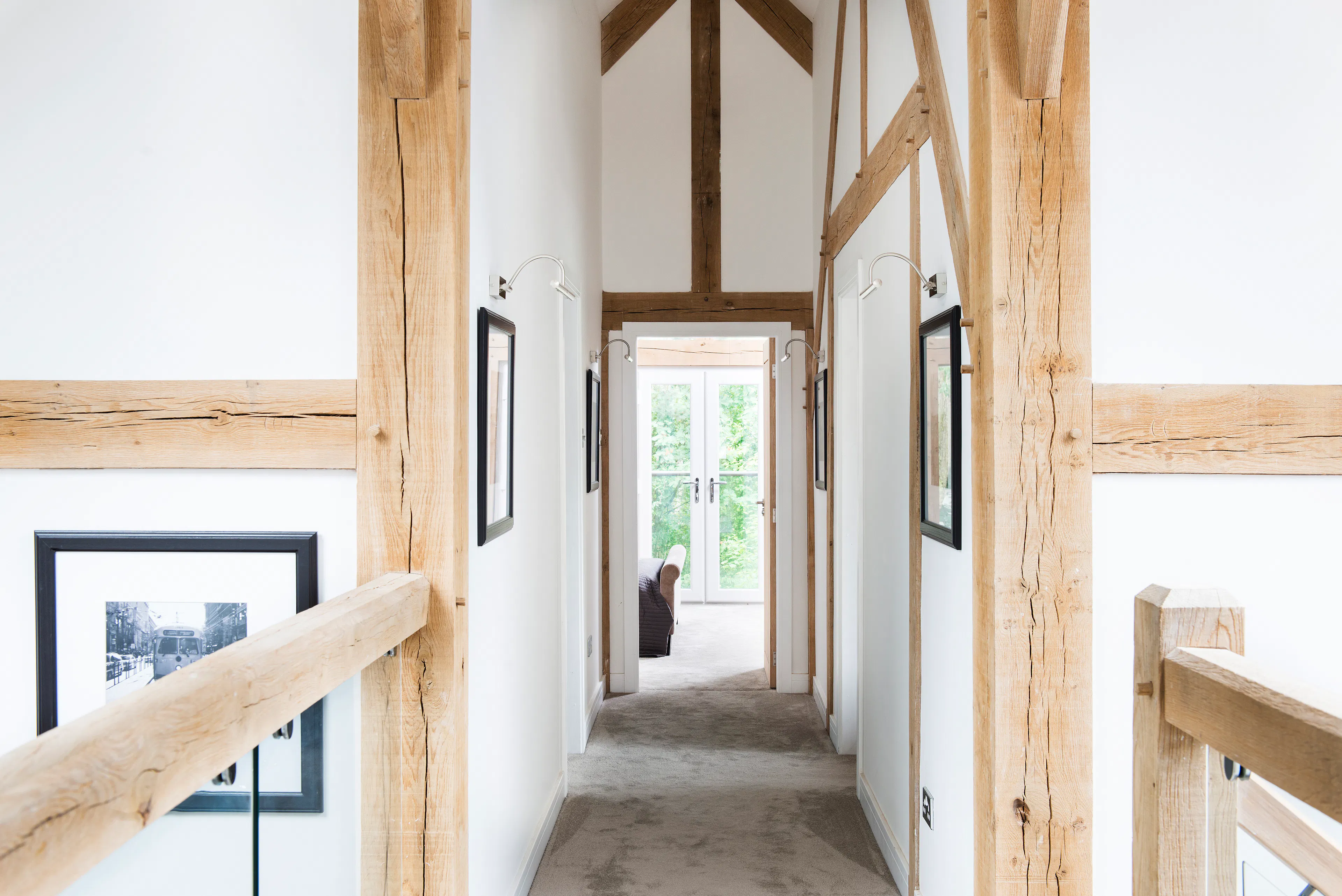 An oak framed walkway landing at the top of the stairs looking down a hallway