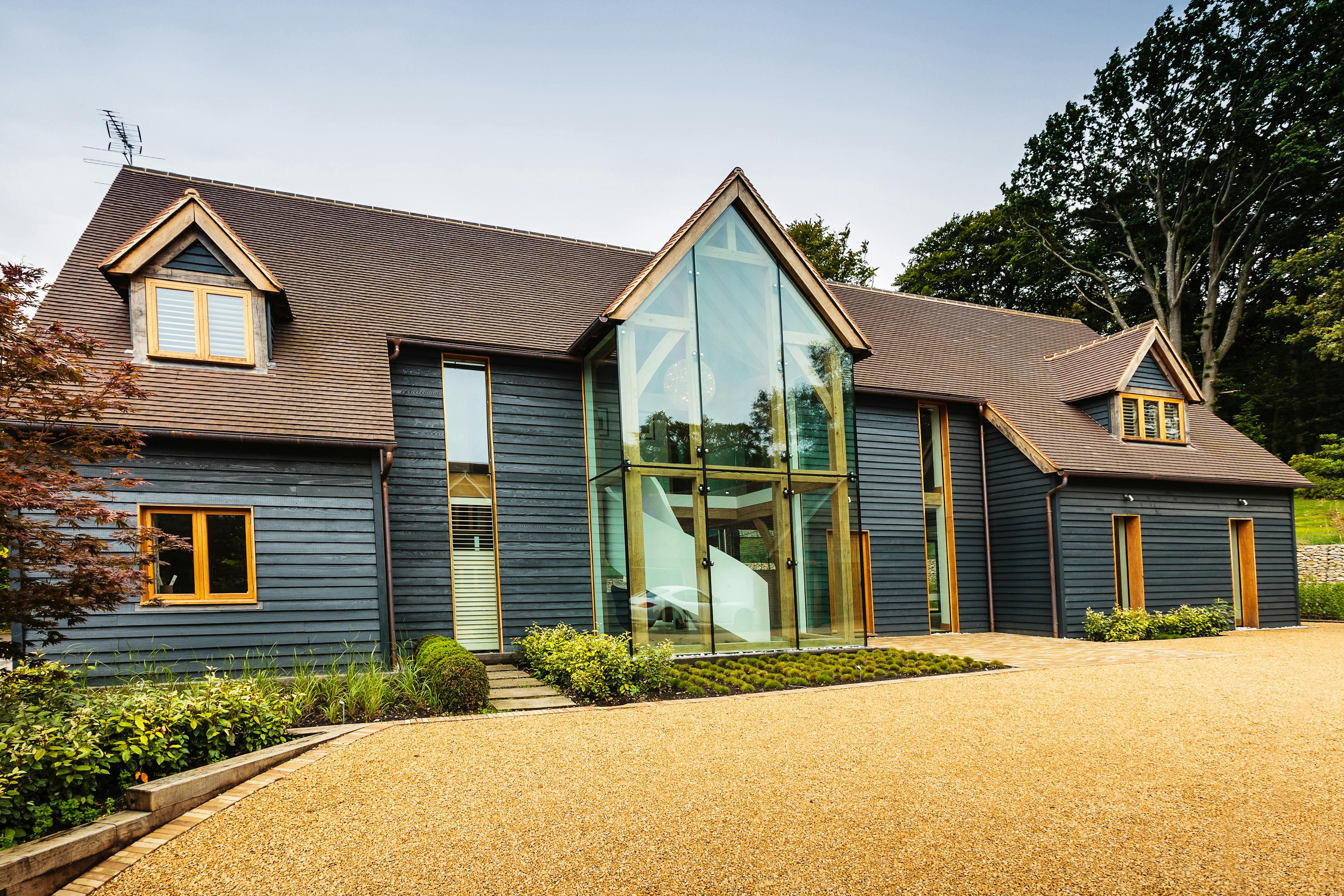 A black clad oak framed house with red roof tiles and a double height glazed entranceway