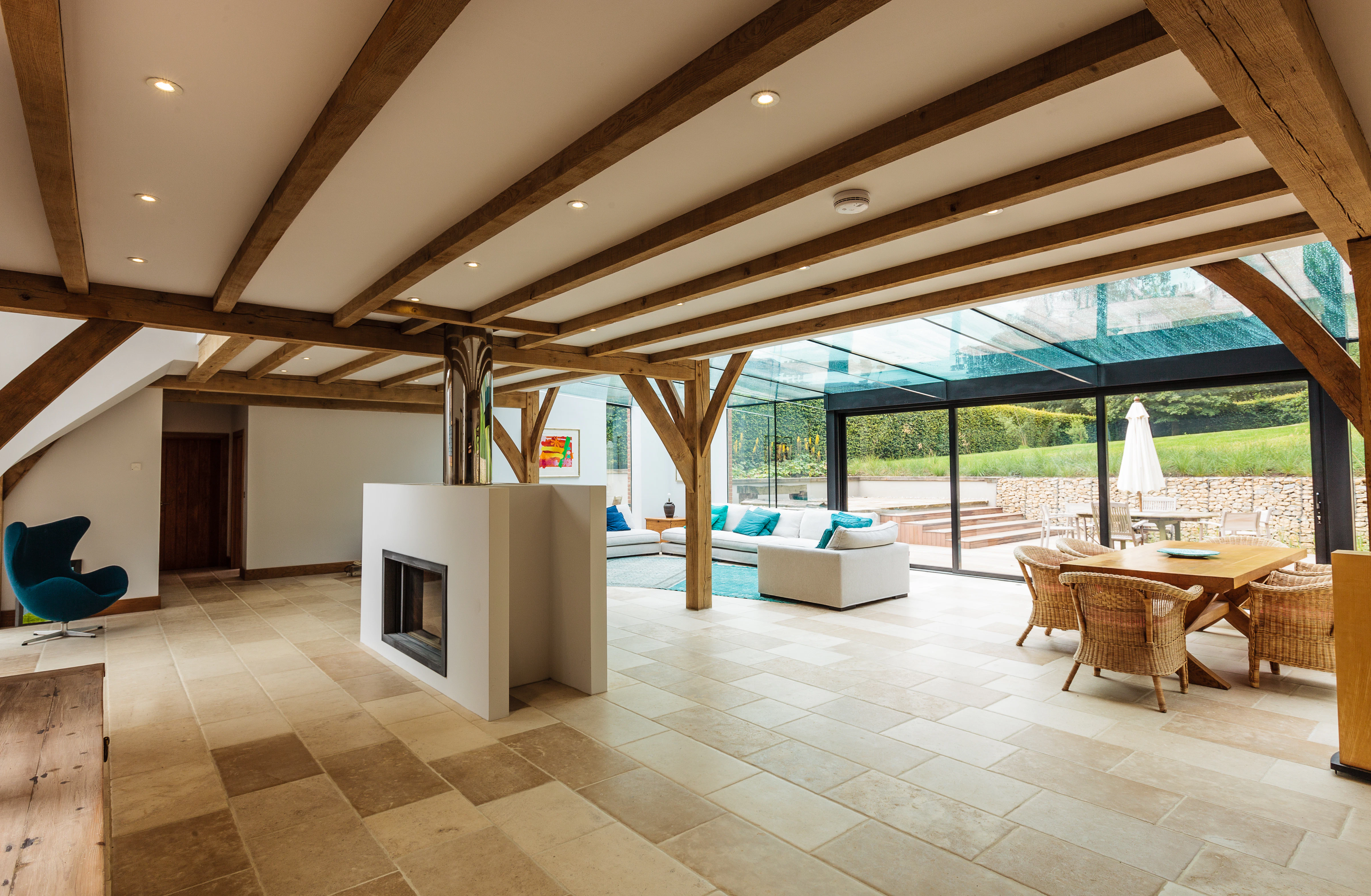 An oak framed living area with dining table, chairs, sofas and a white fireplace with a modern glazed extension