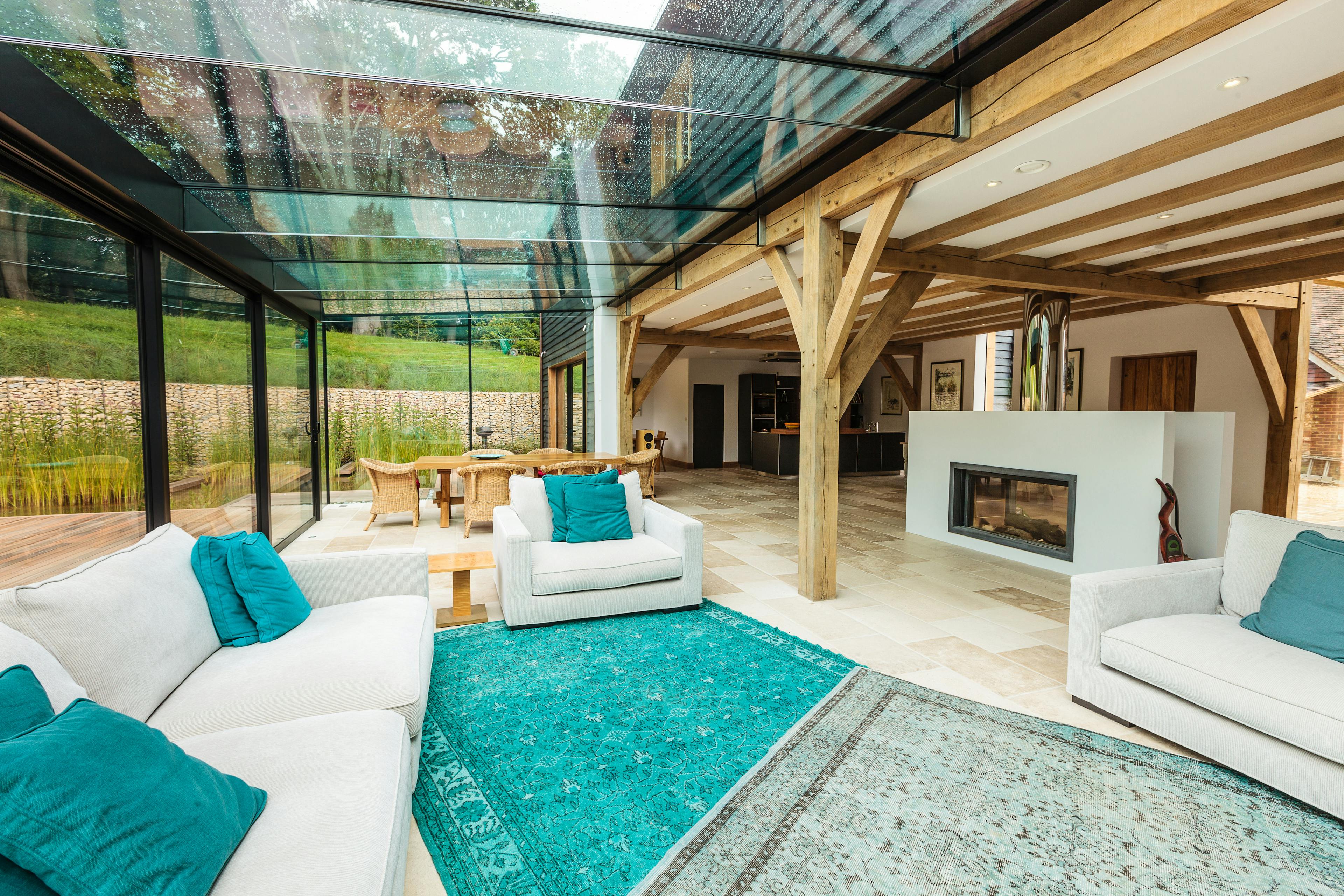 An oak framed living area with dining table and chairs, sofas and a fireplace with a modern glazed extension