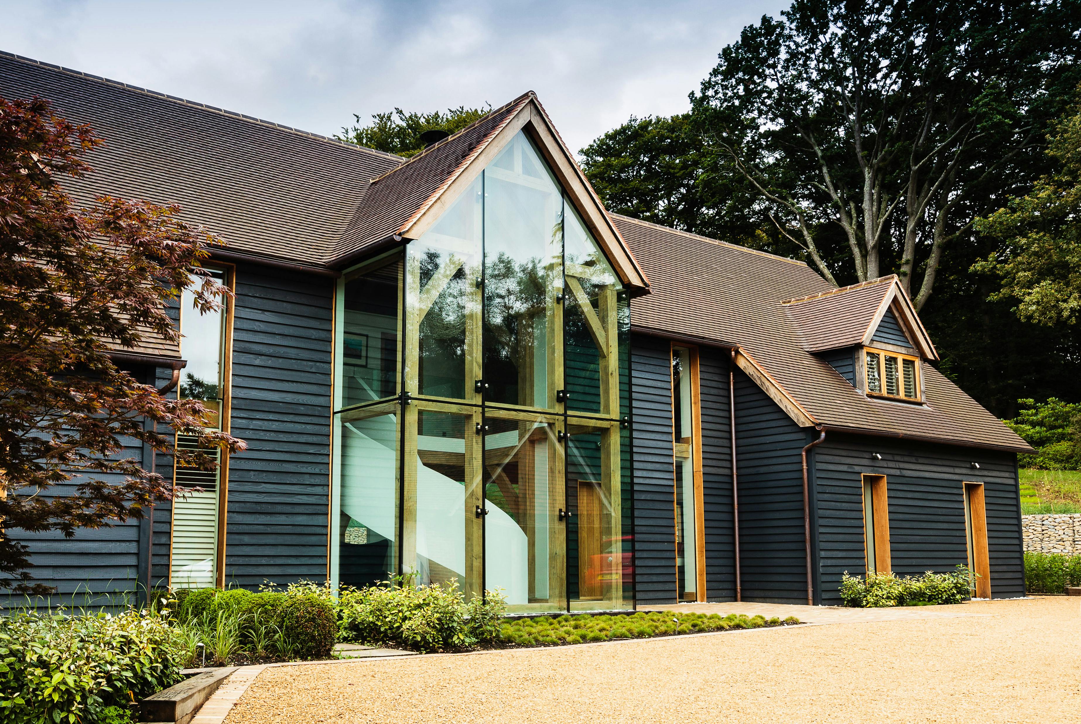 A black clad oak framed house with red roof tiles and a double height glazed entranceway