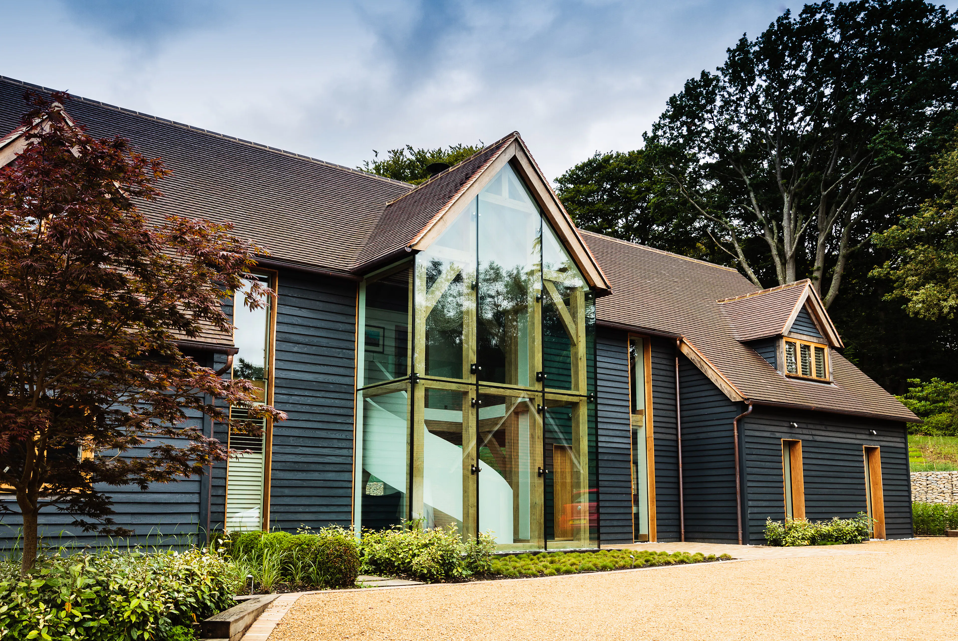 A black clad oak framed house with red roof tiles and a double height glazed entranceway