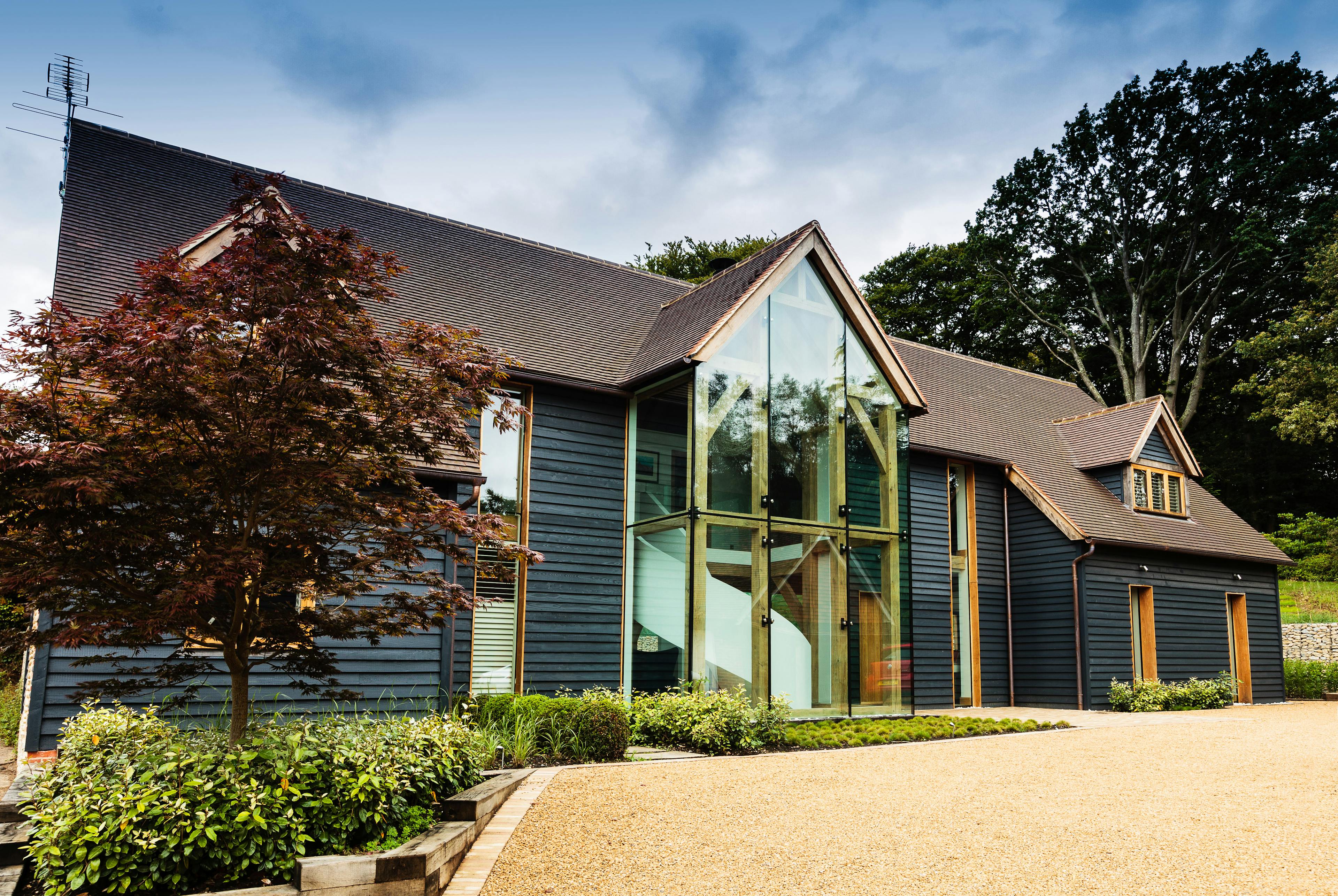 A black clad oak framed house with red roof tiles and a double height glazed entranceway