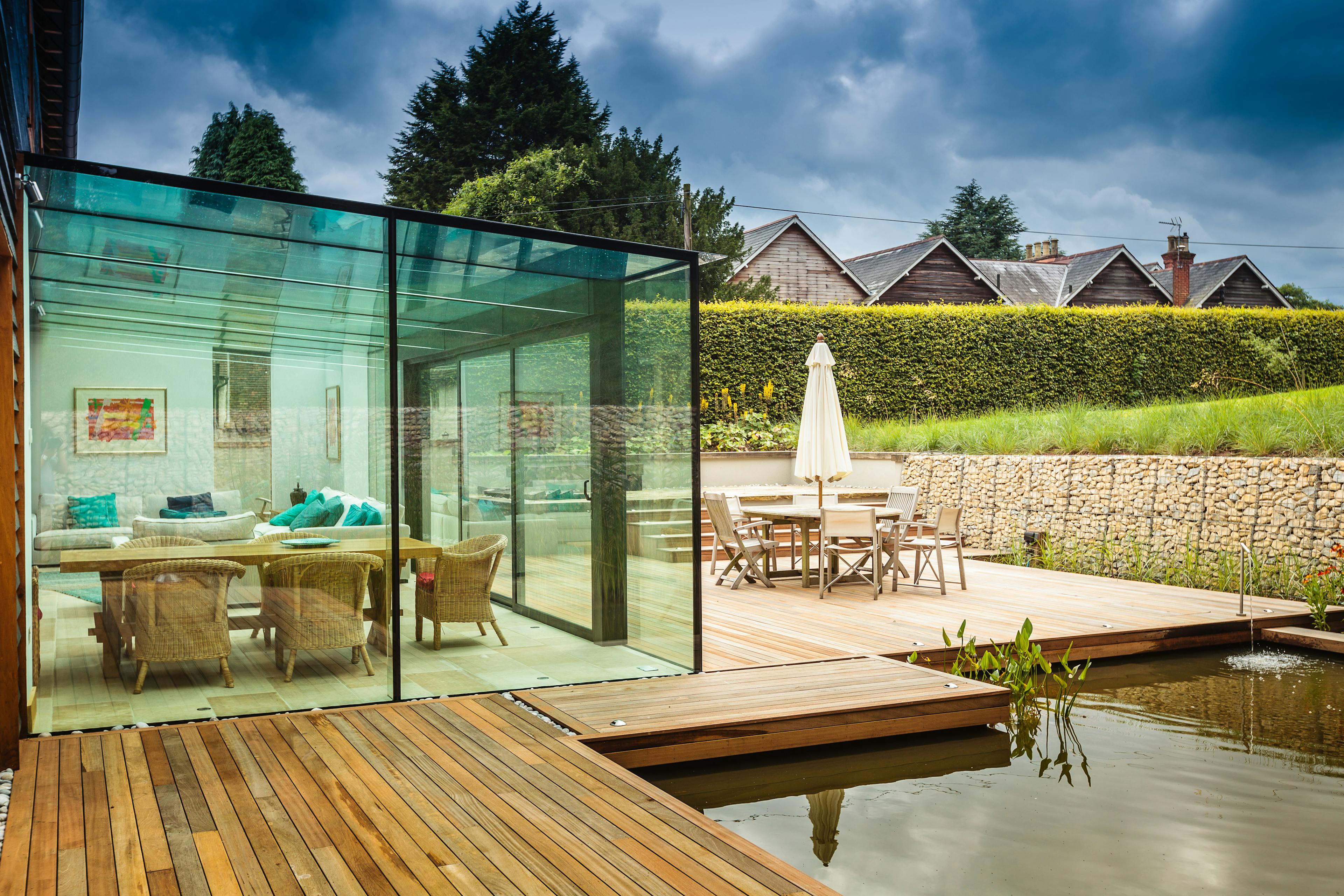A patio with outdoor table and chairs and large pond next to a modern glazed extension