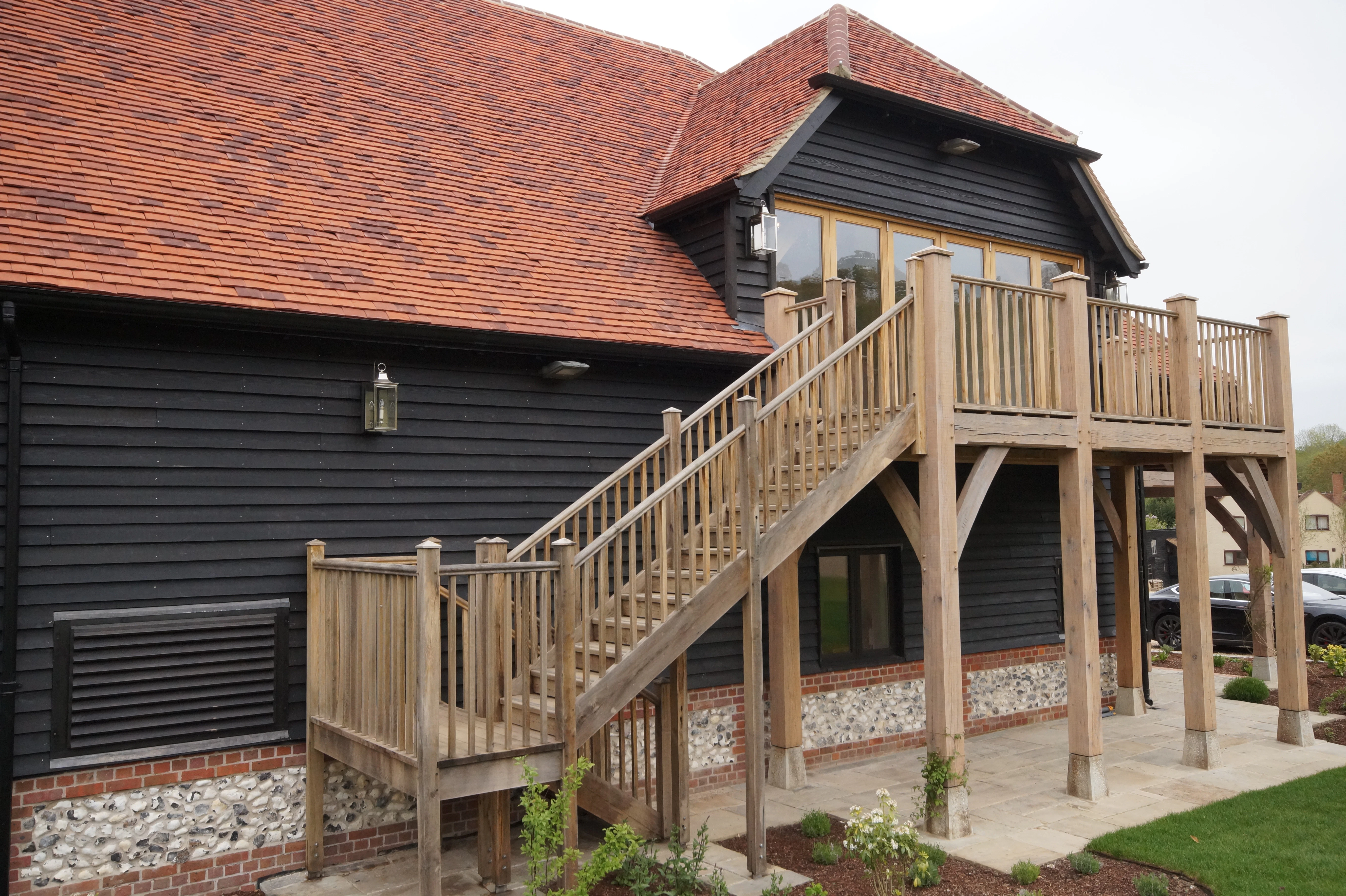 An oak framed balcony on a black clad building with red roof tiles