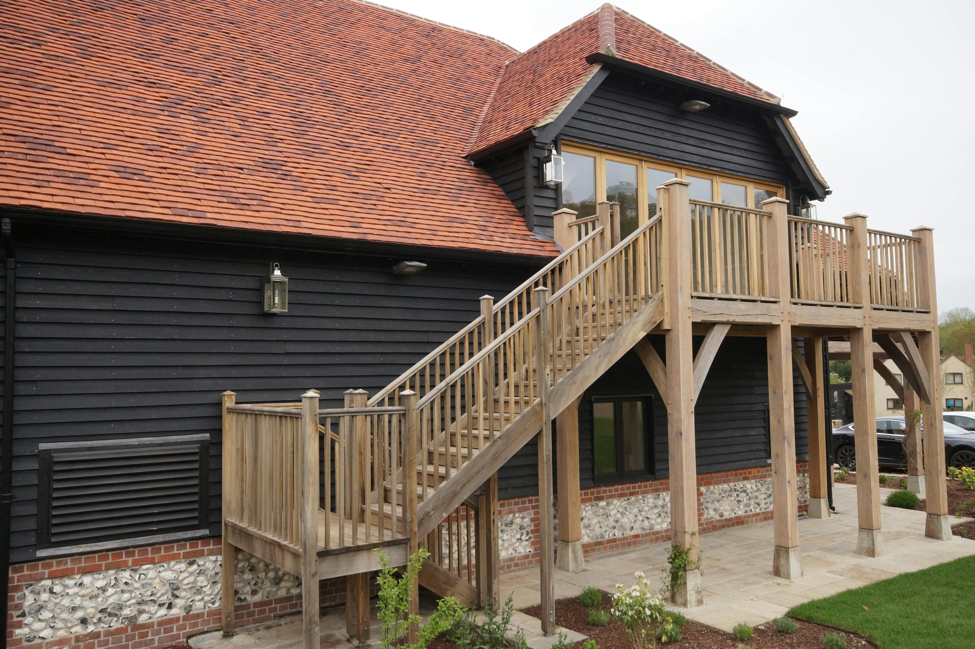 An oak framed balcony on a black clad building with red roof tiles