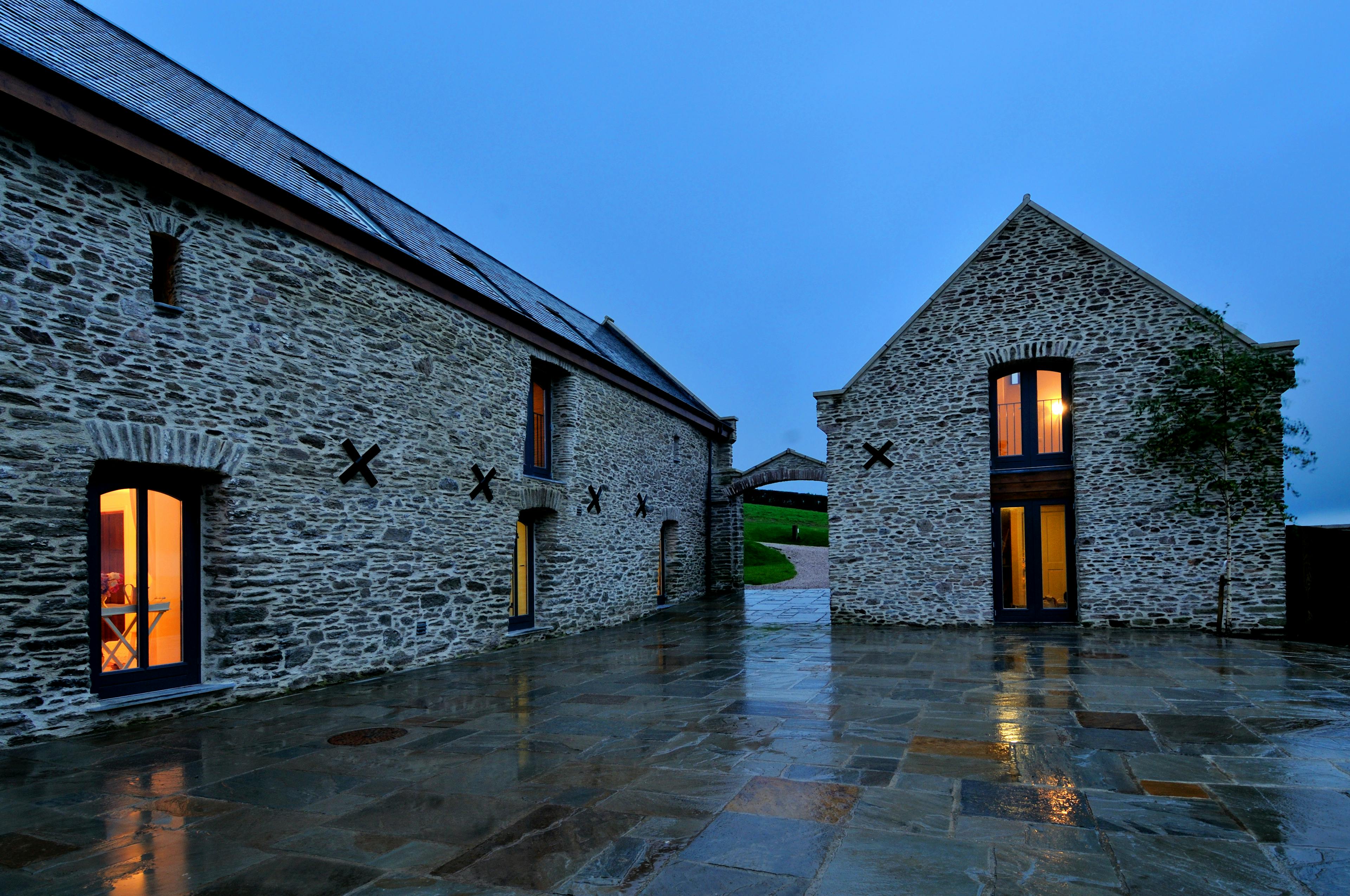 At dusk light shines from the windows of a stone clad barn converted to a home