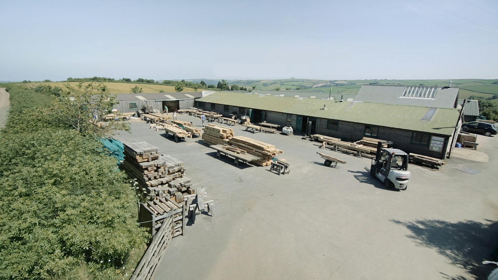 An aerial view of a workshop and timber framing yard with green hills in the distance