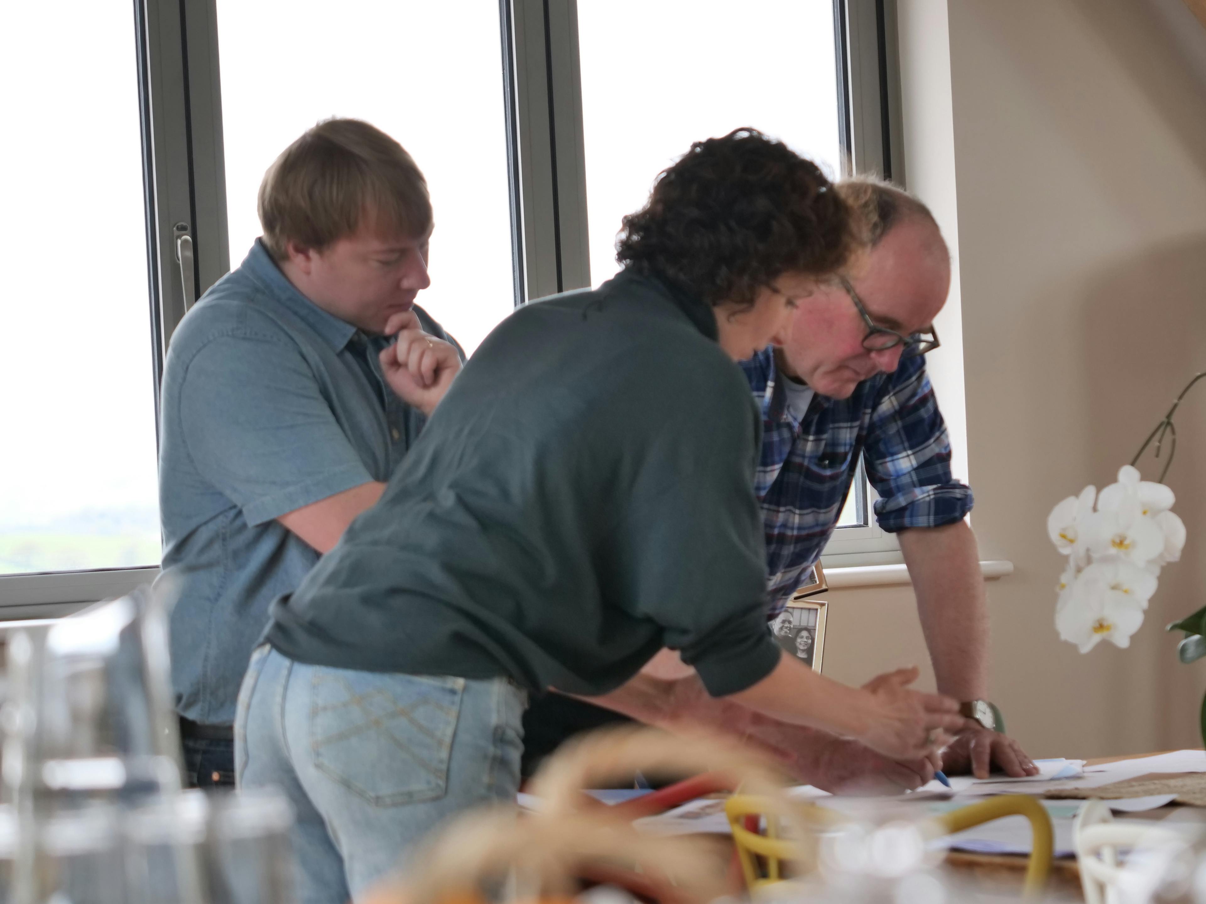 Three people  in conversation lean over a table looking at paperwork