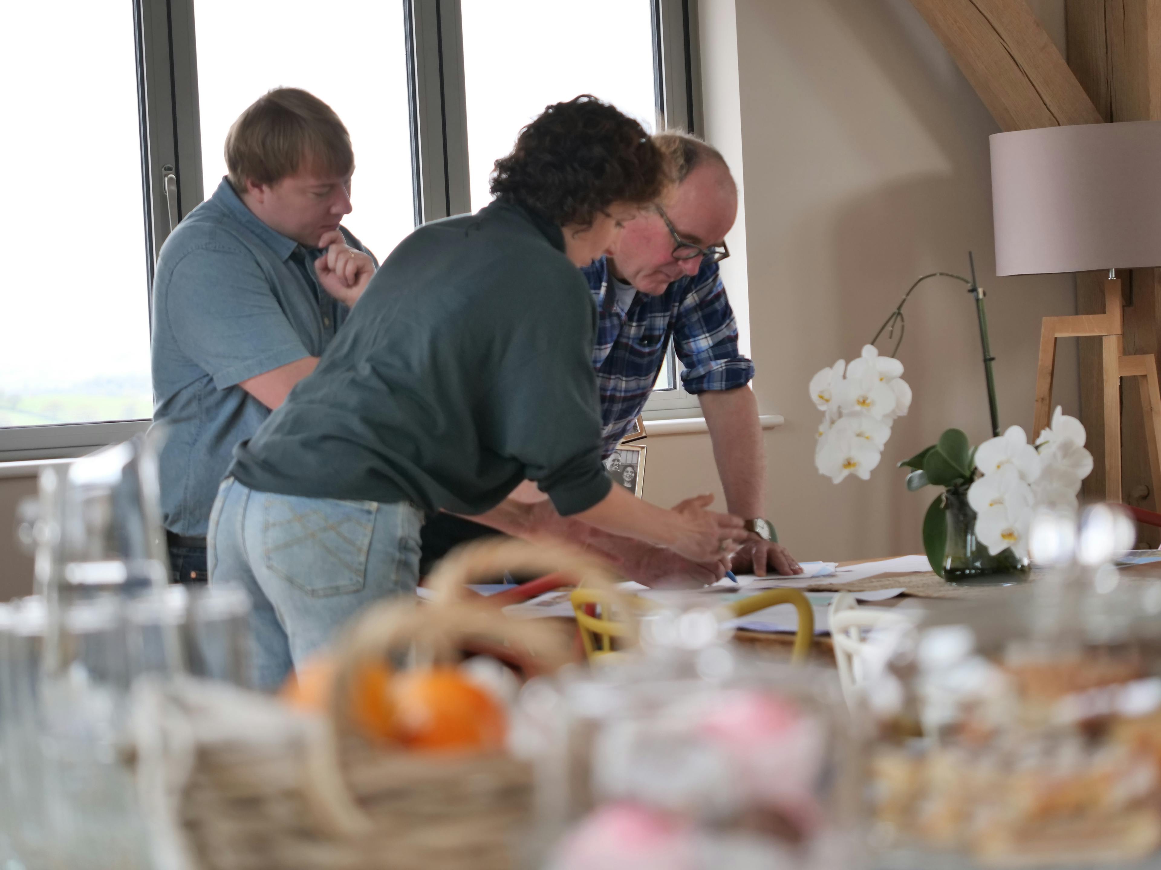 Three people in conversation lean over a table looking at paperwork