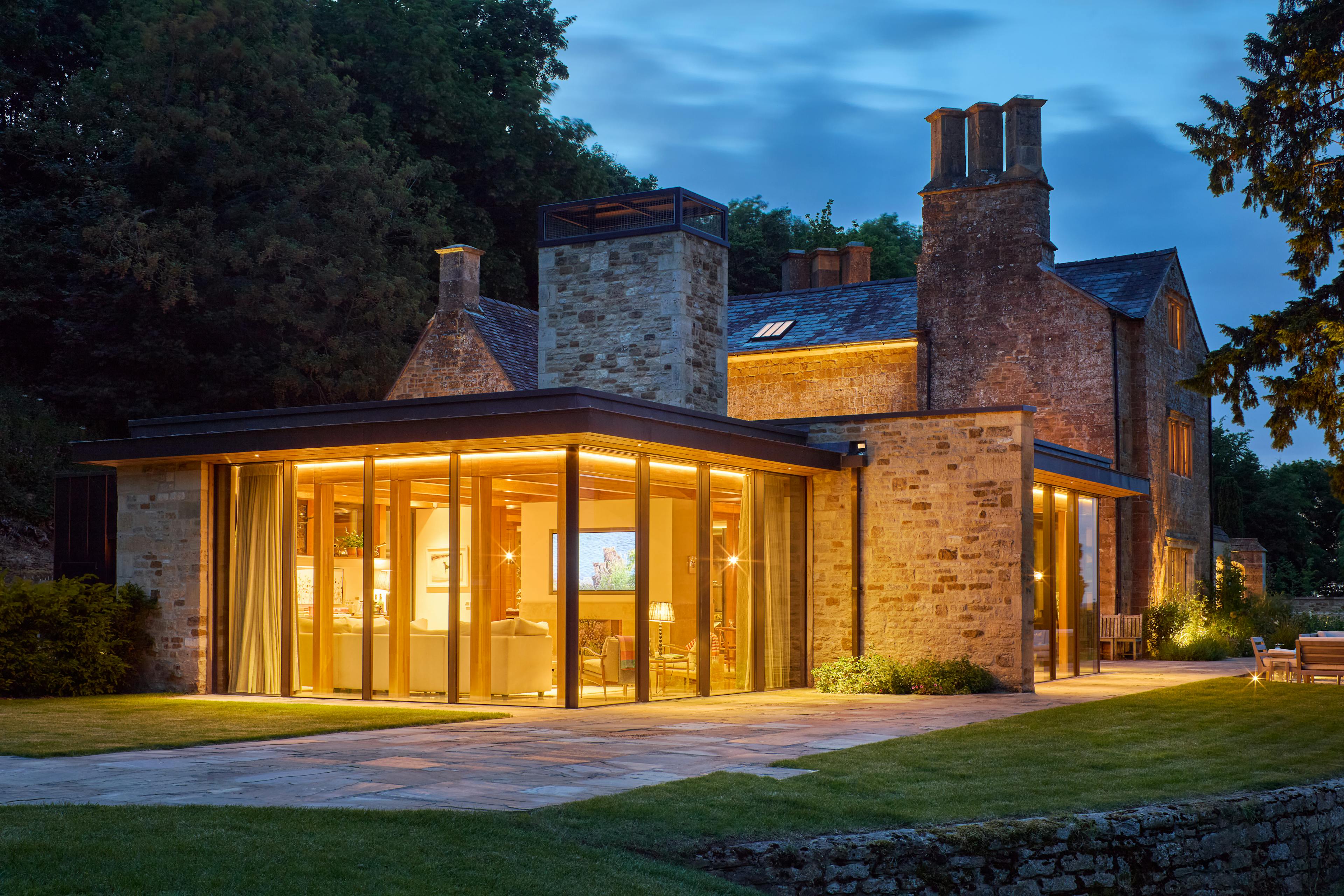 Exterior of an oak glulam extension to a listed manor house taken at dusk with the lights on