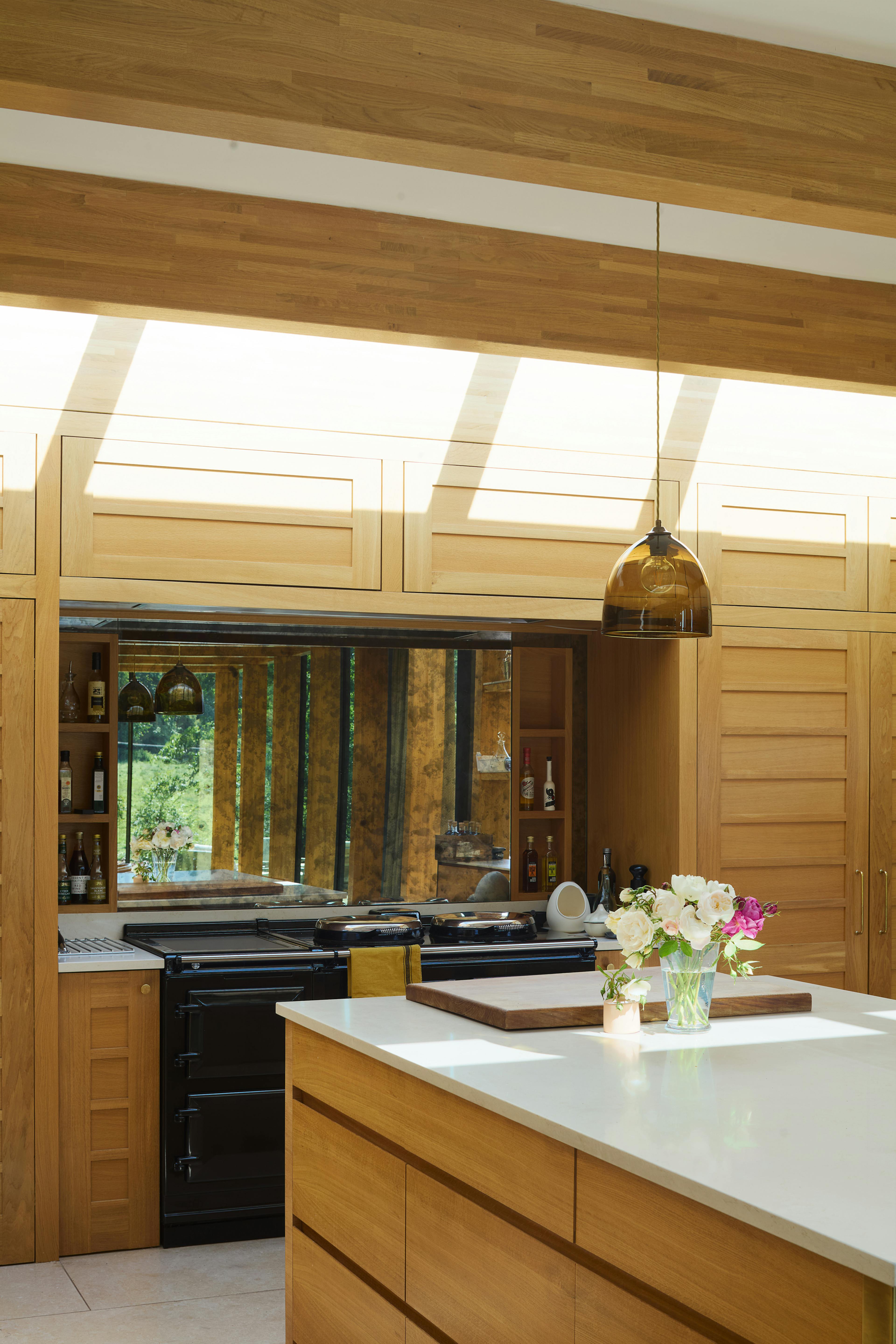 The kitchen of an oak glulam extension to a listed manor house with sunshine coming through the skylights