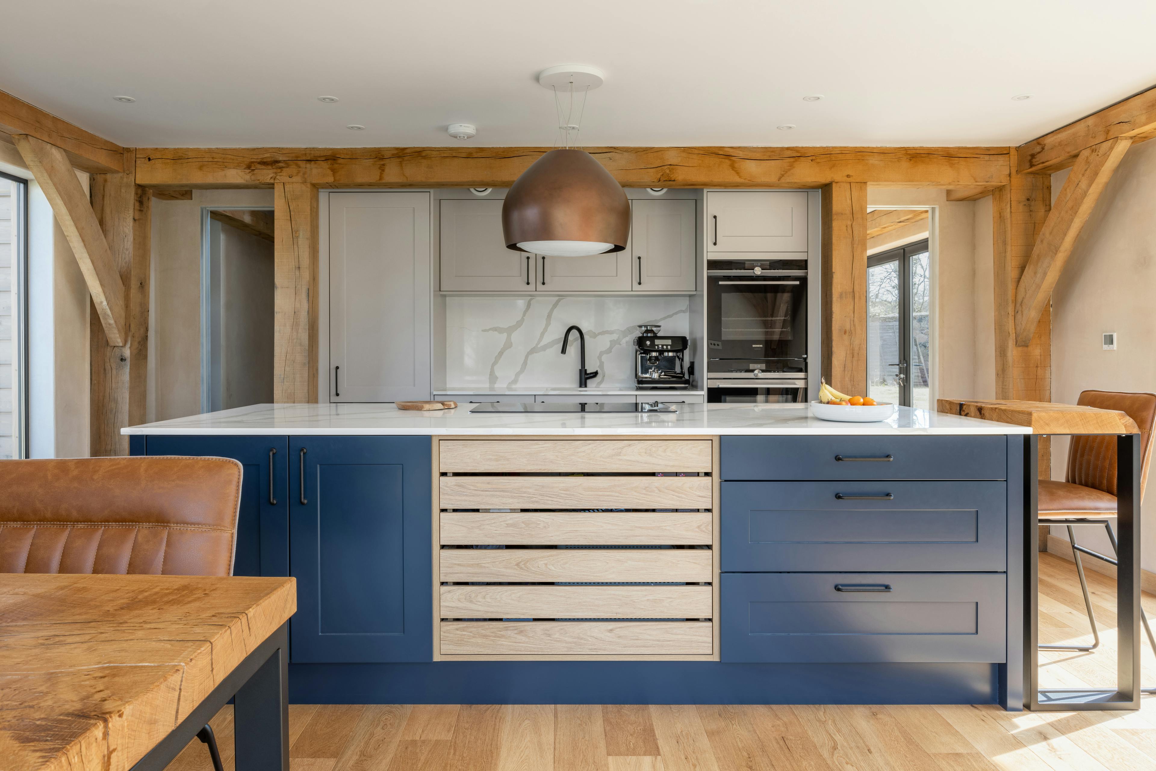 An oak framed kitchen with a blue painted island and wooden dining table
