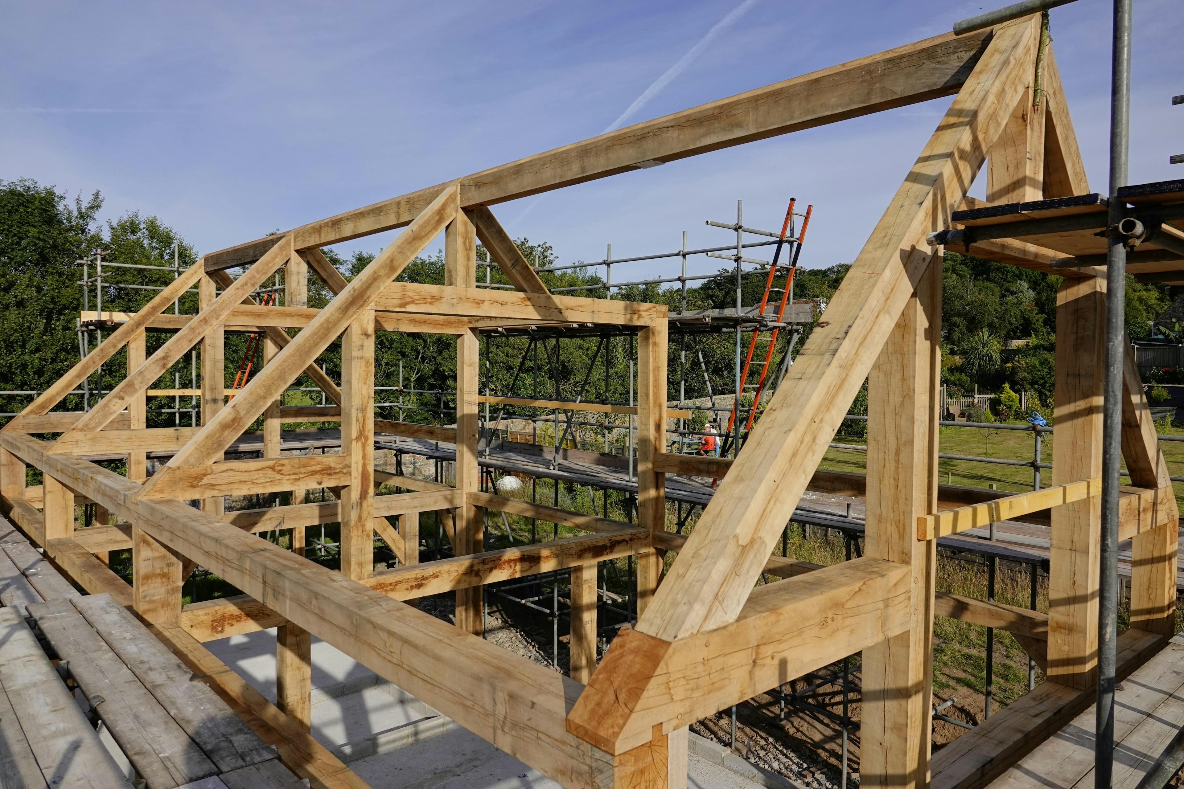 An oak frame during installation on a construction site with blue skies behind