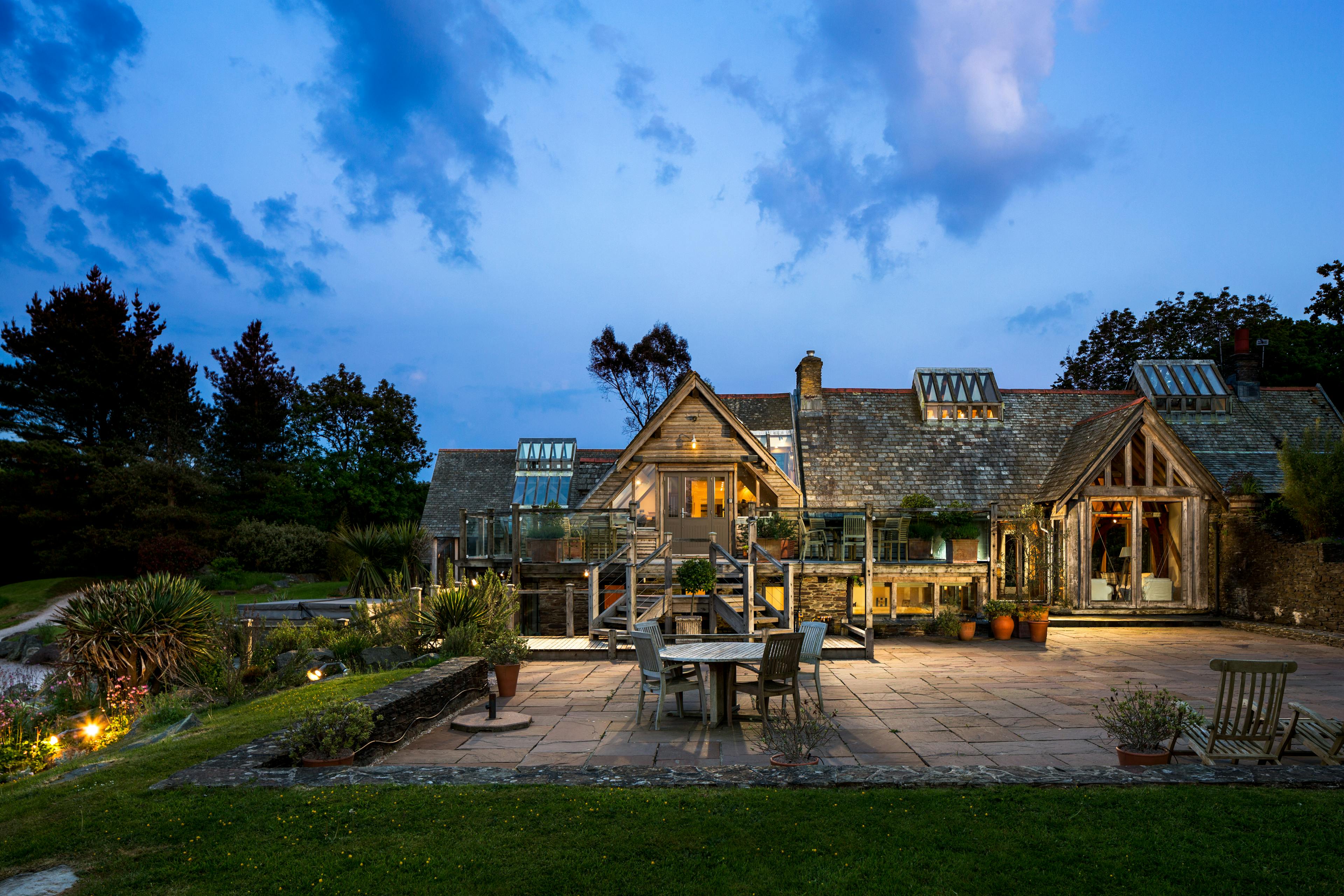 The rear of a large oak framed building with a patio and pond at dusk