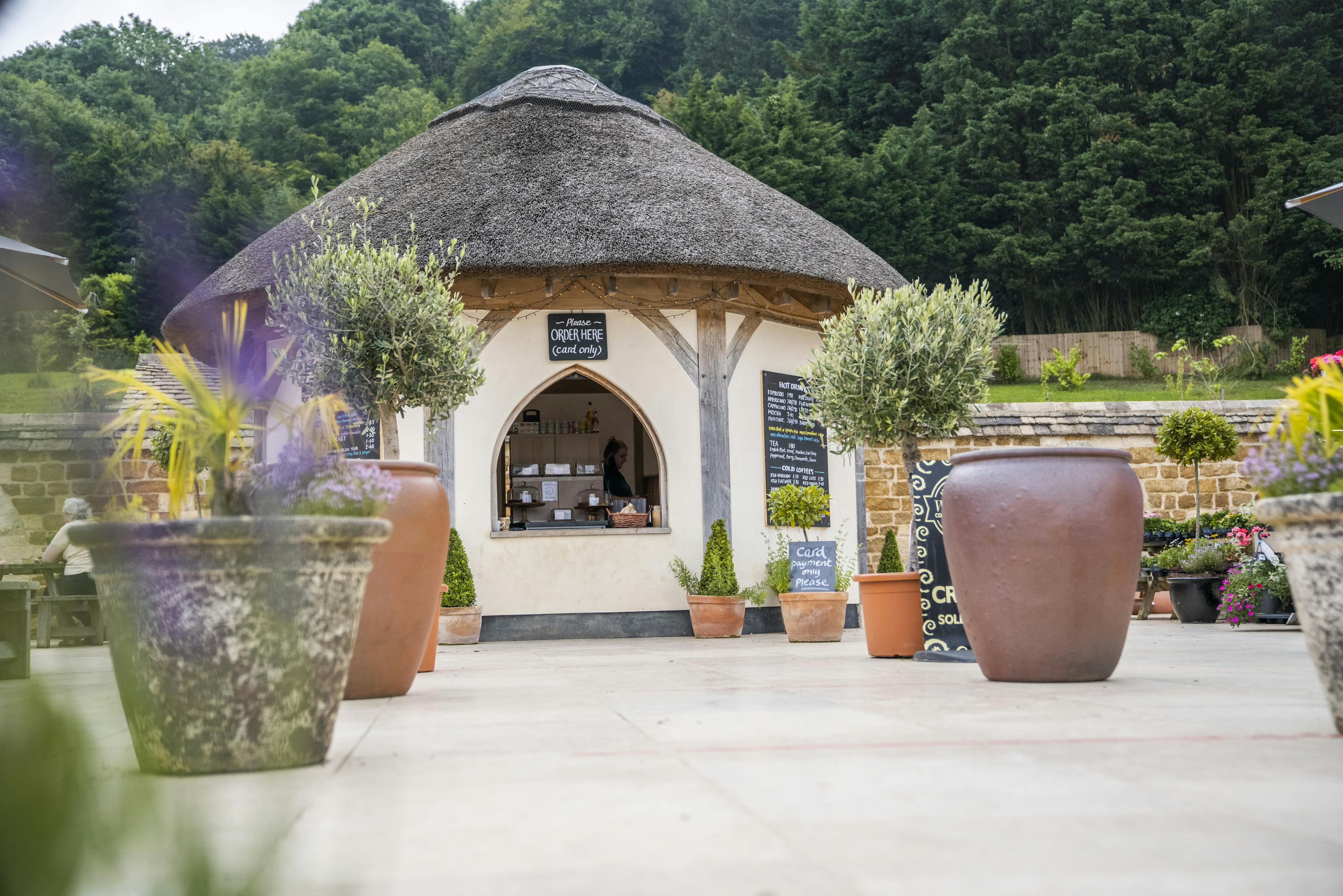 A small round oak framed building with a thatched roof on a paved courtyard