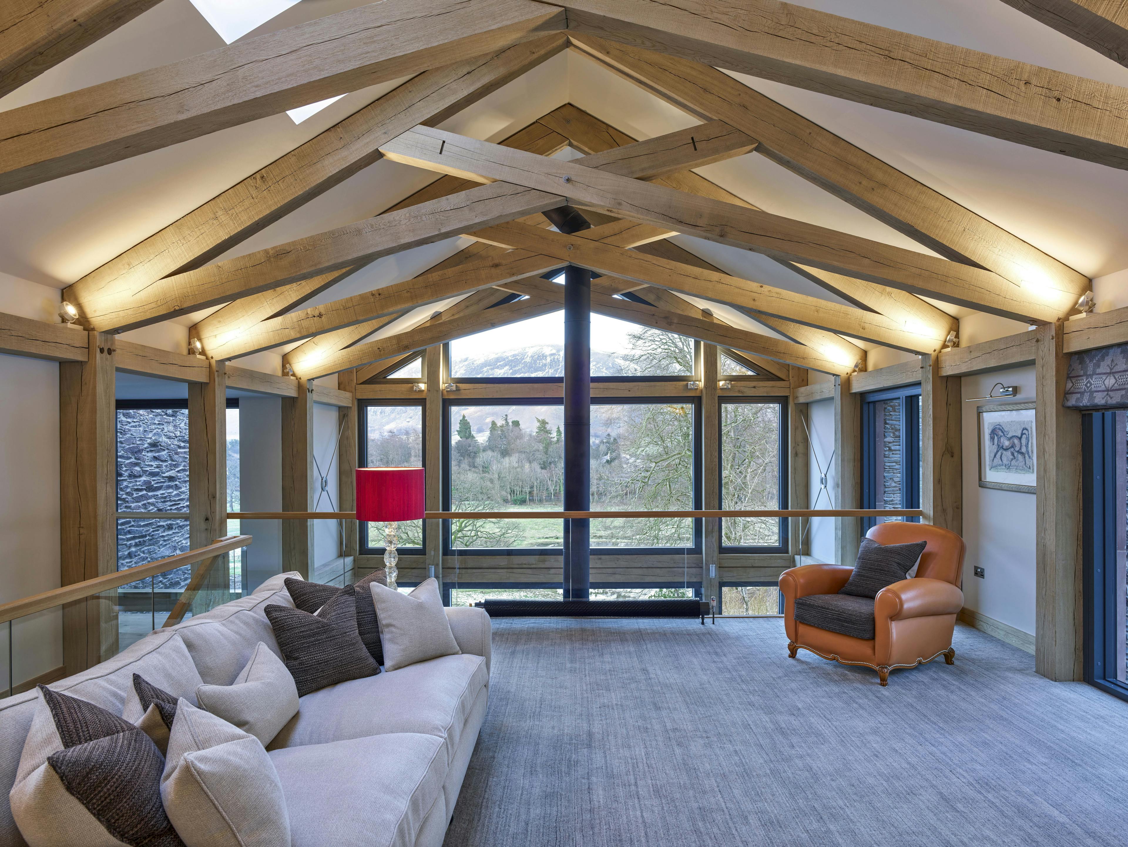 A mezzanine sitting area with sofas and an orange armchair and an oak framed scissor truss