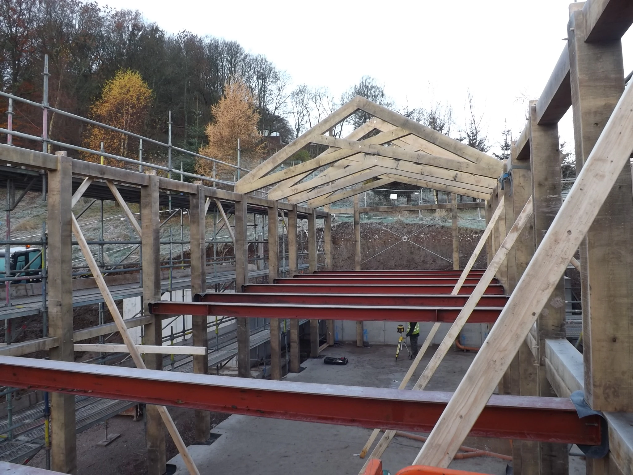 An oak frame with scissor trusses and a red steel frame on a construction site during installation