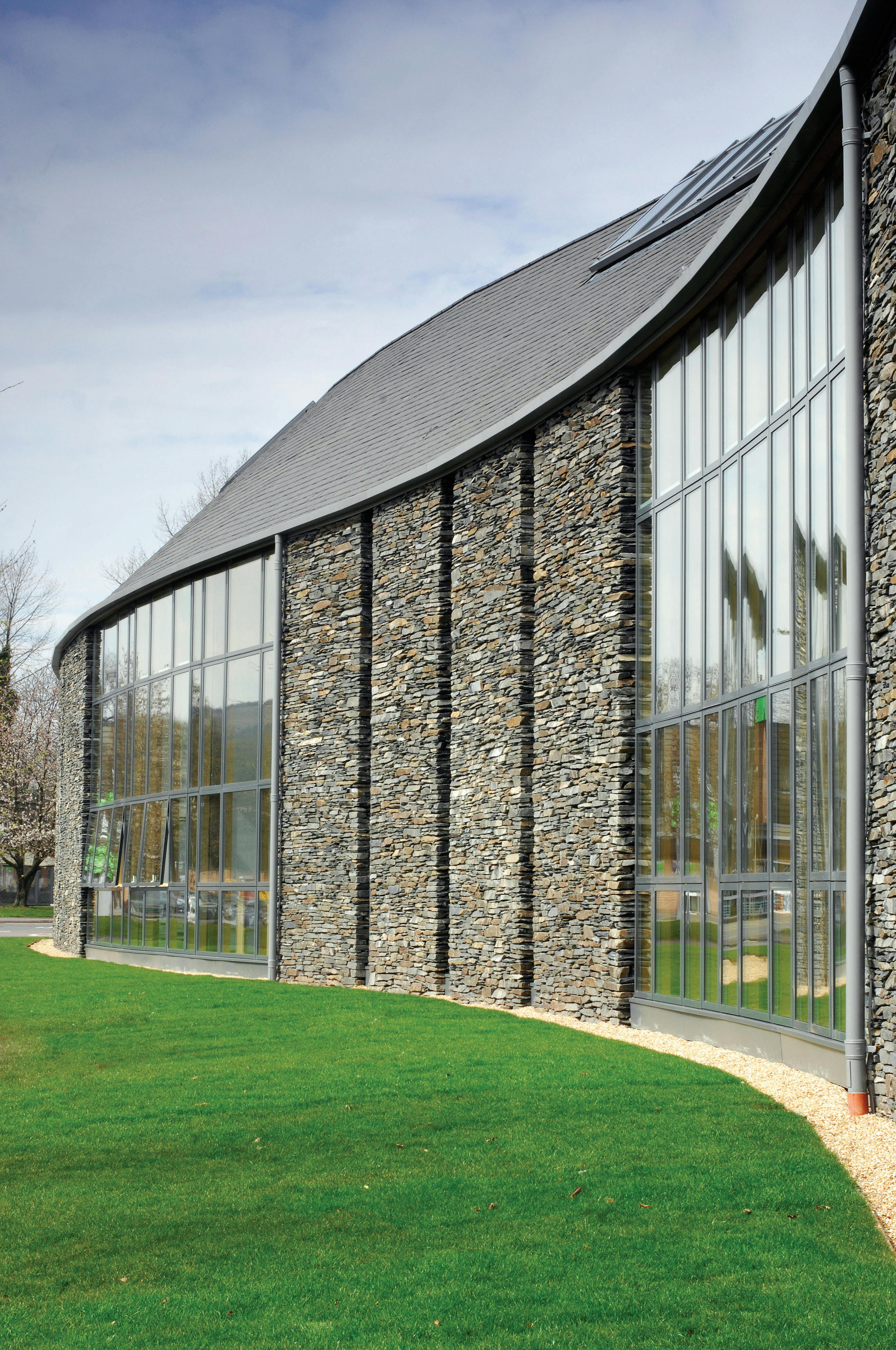A stone clad large curved building with large glazed windows