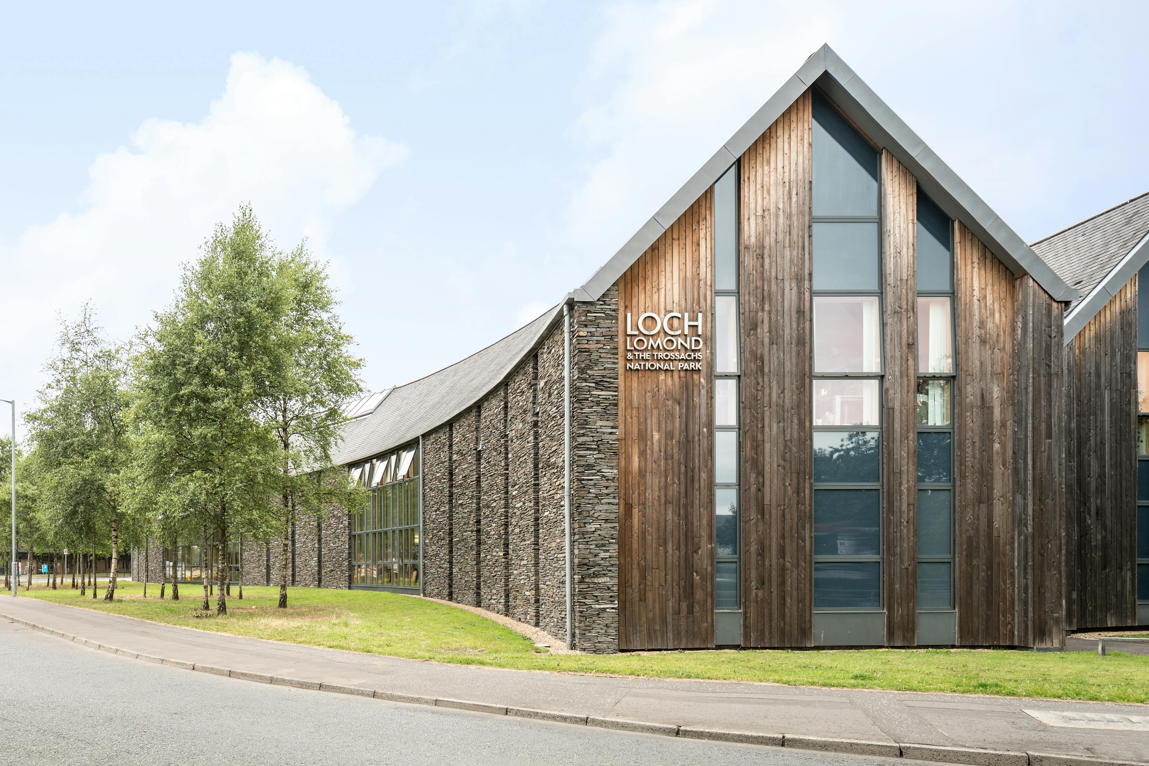 A stone and timber clad large curved building with large glazed windows
