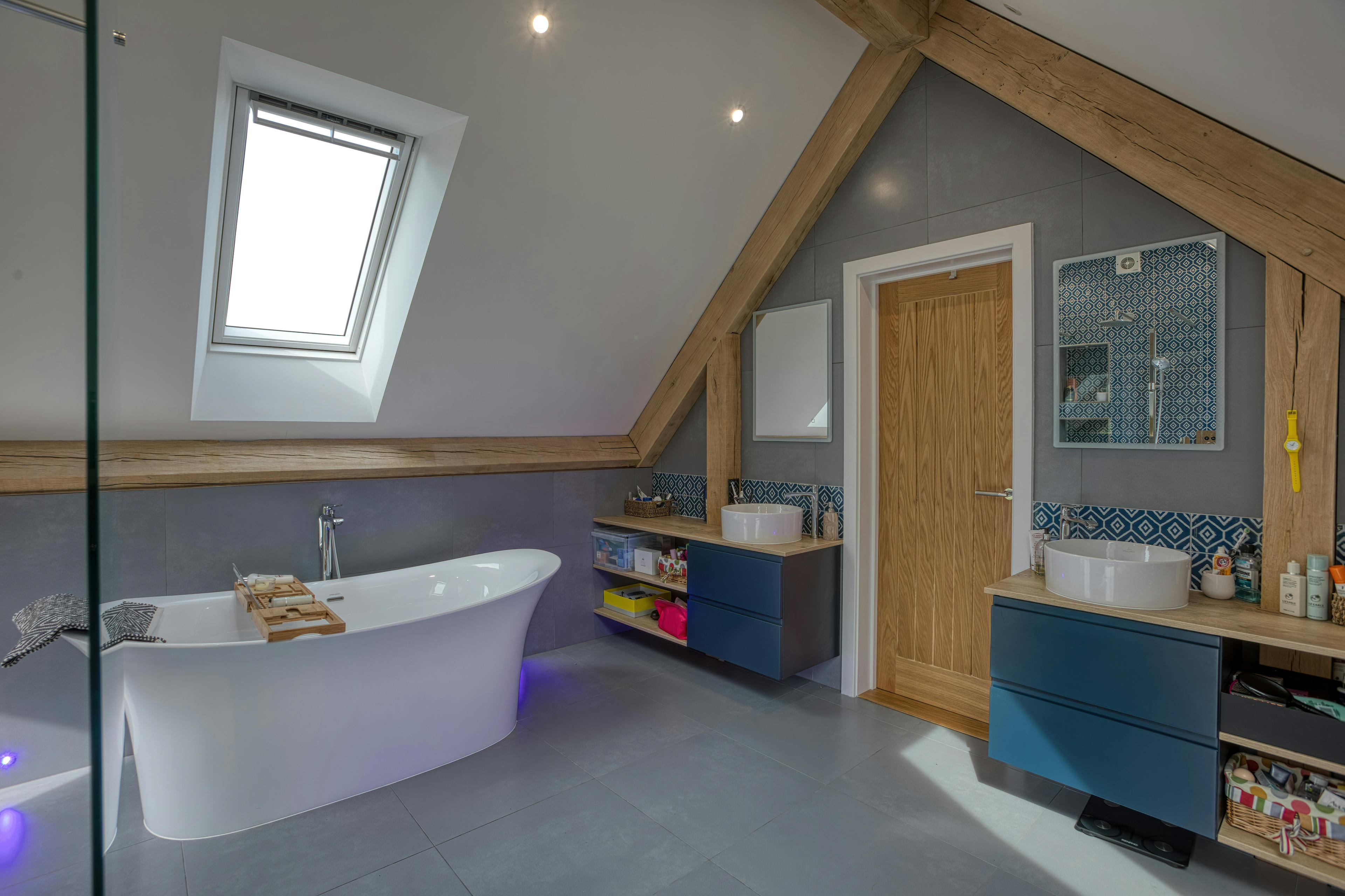 Interior view of a contemporary large bathroom featuring exposed oak-frame beams and a free standing bath