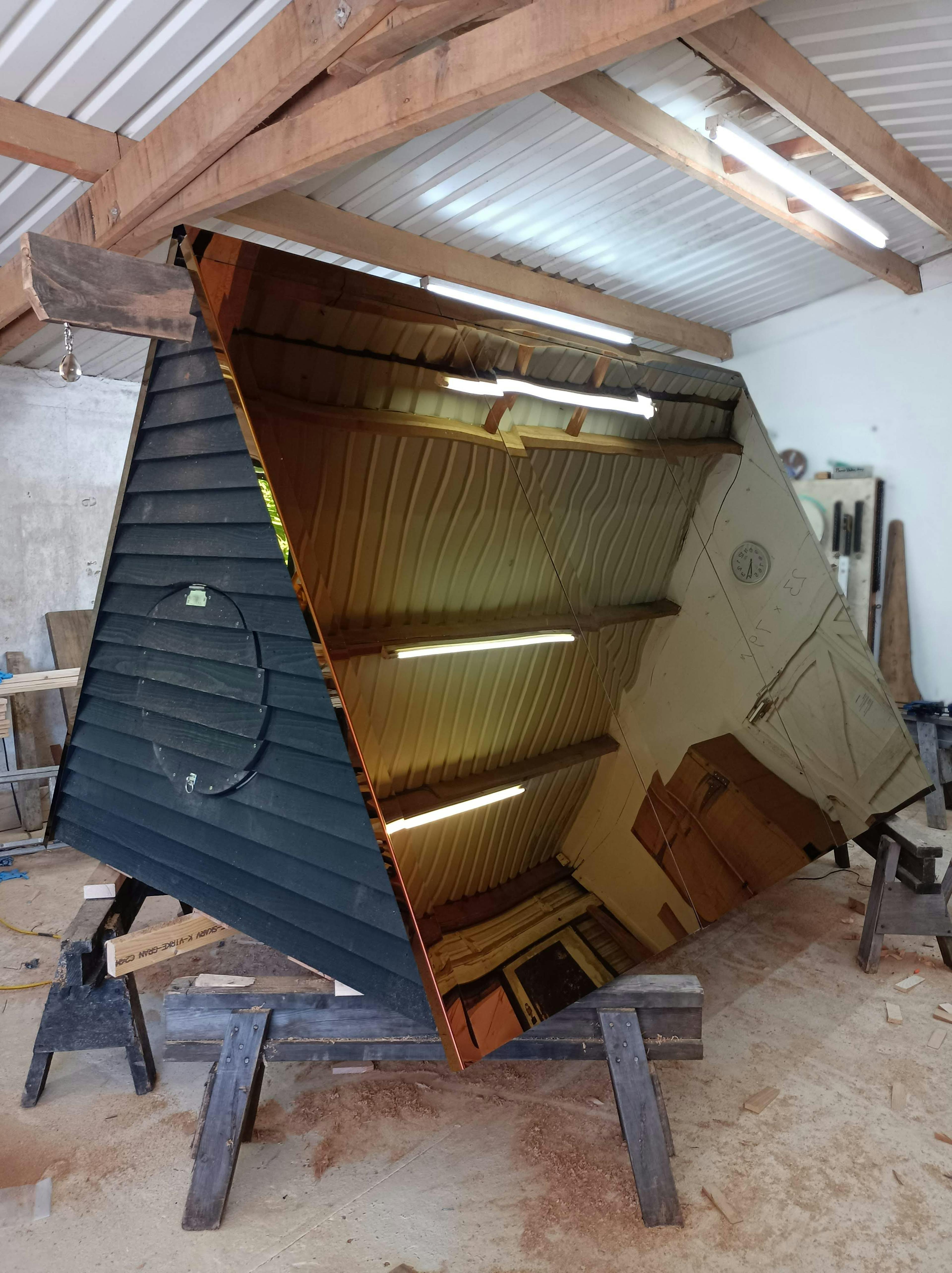 In a workshop an oak framed cabin roof with reflective steel is constructed