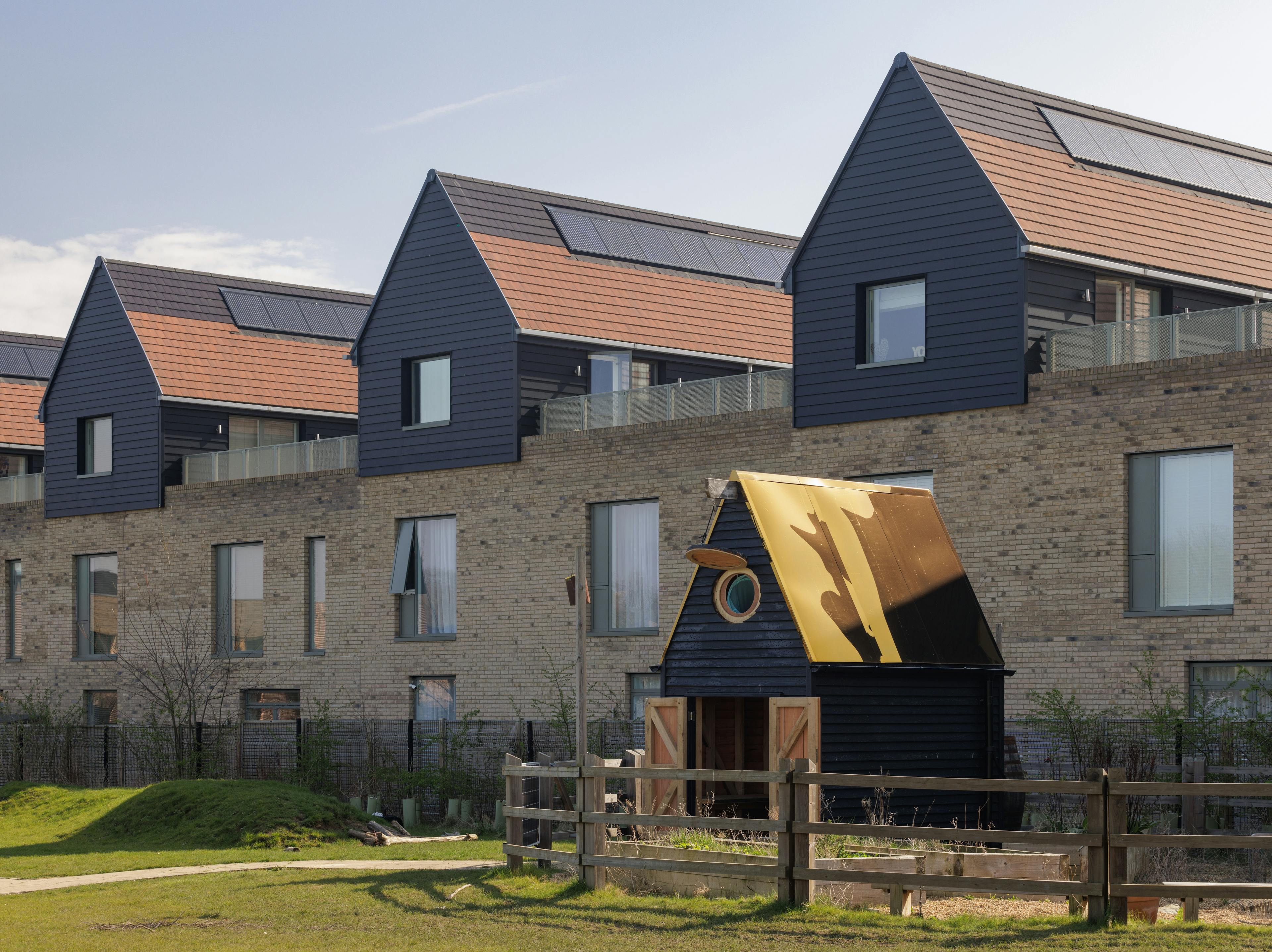 a black clad oak framed cabin with reflective steel roof next to some housing